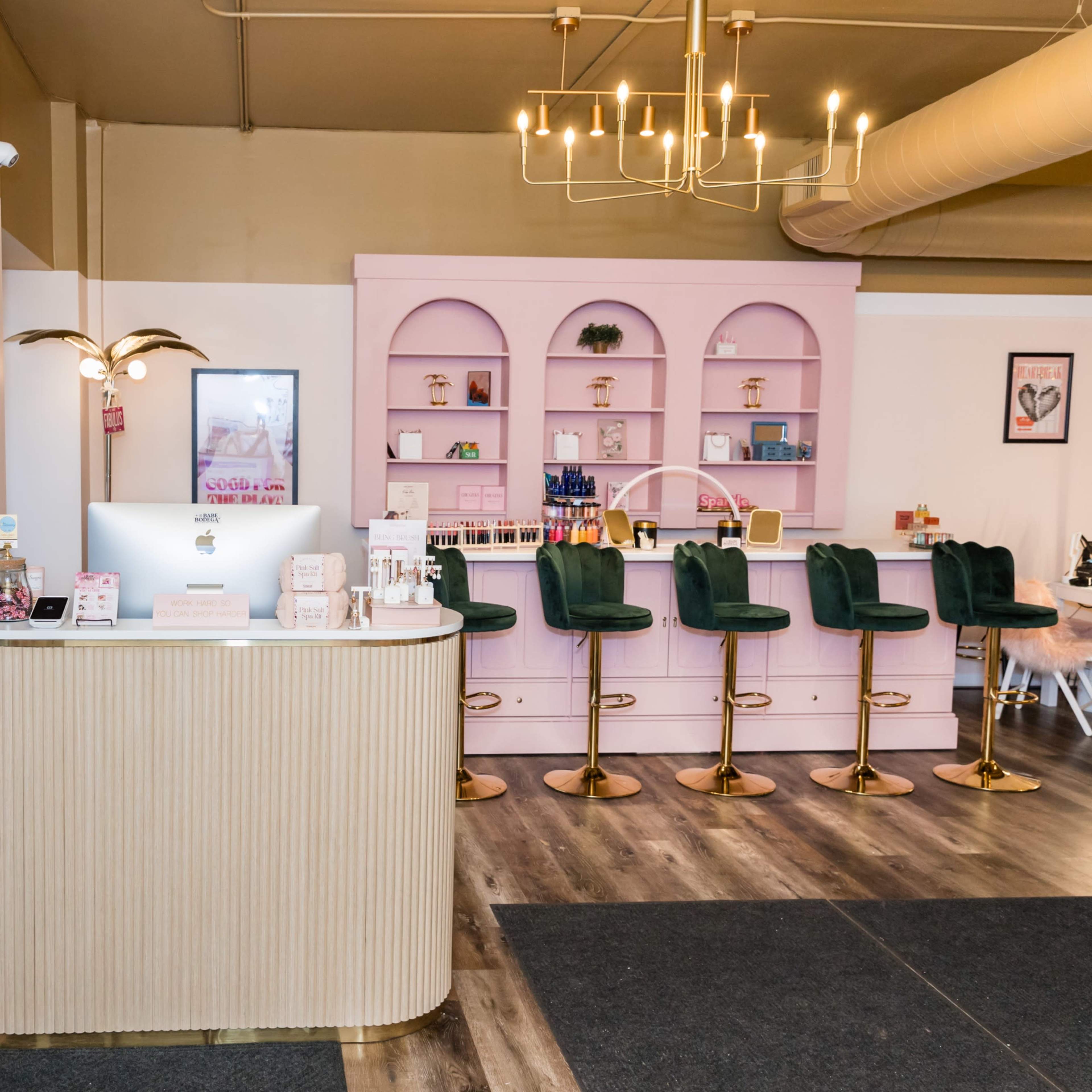 A brightly lit interior featuring a reception desk with a computer and a pink-themed bar area with green stools.