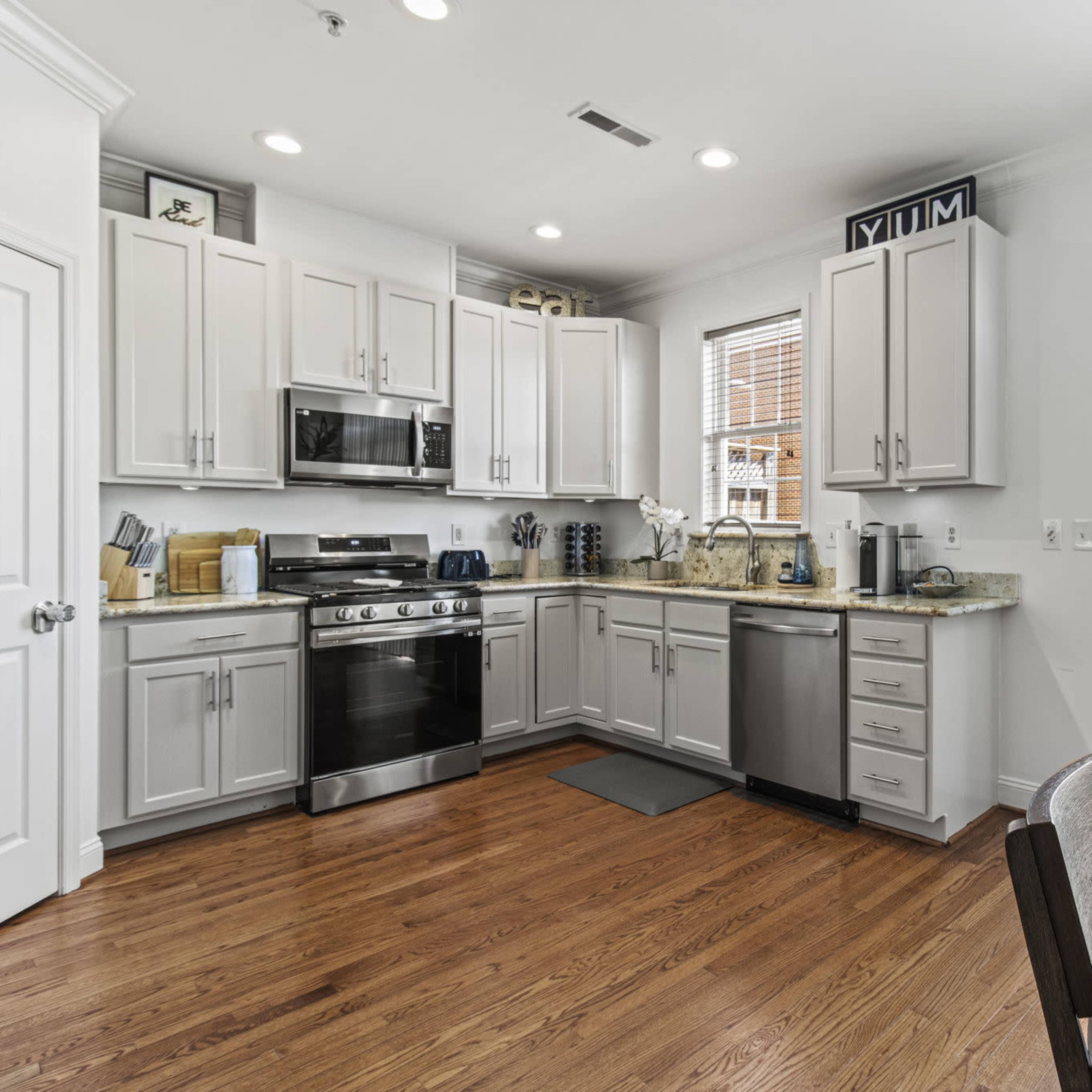 A modern kitchen featuring stainless steel appliances, light cabinetry, and a dining area with a wooden table.