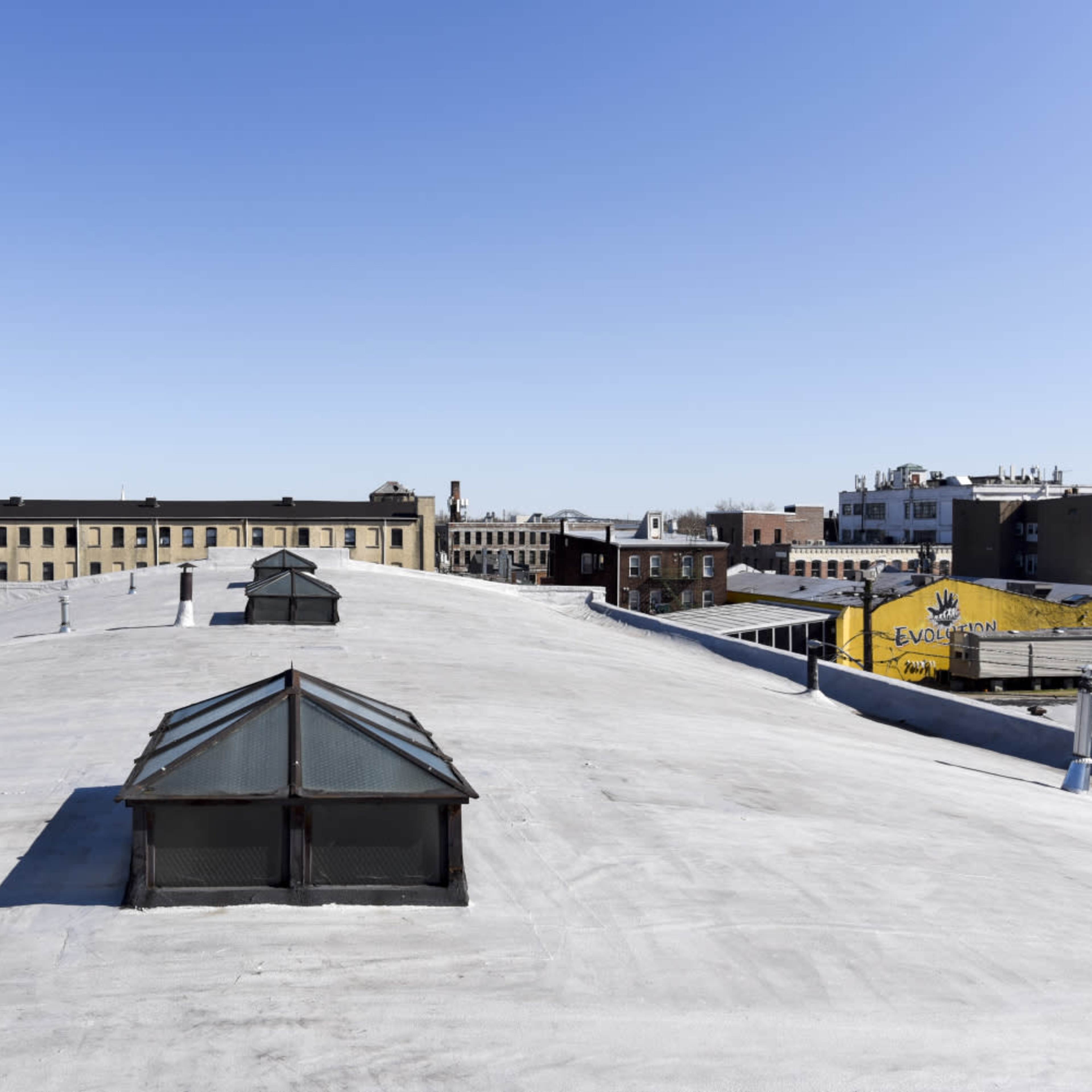 A flat rooftop with several skylights, overlooking city buildings and a clear blue sky in the background.