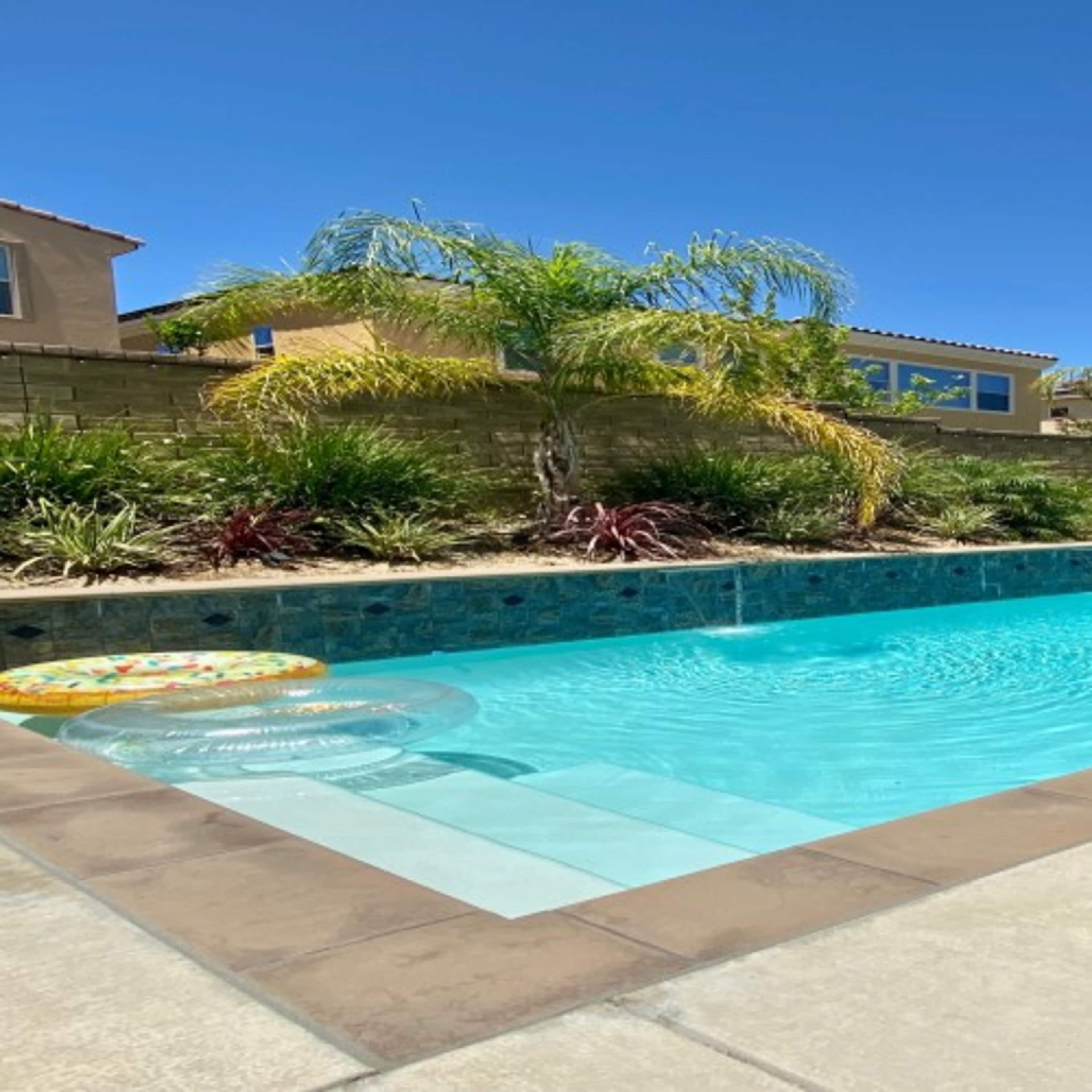 A swimming pool surrounded by landscaped greenery and houses in the background.