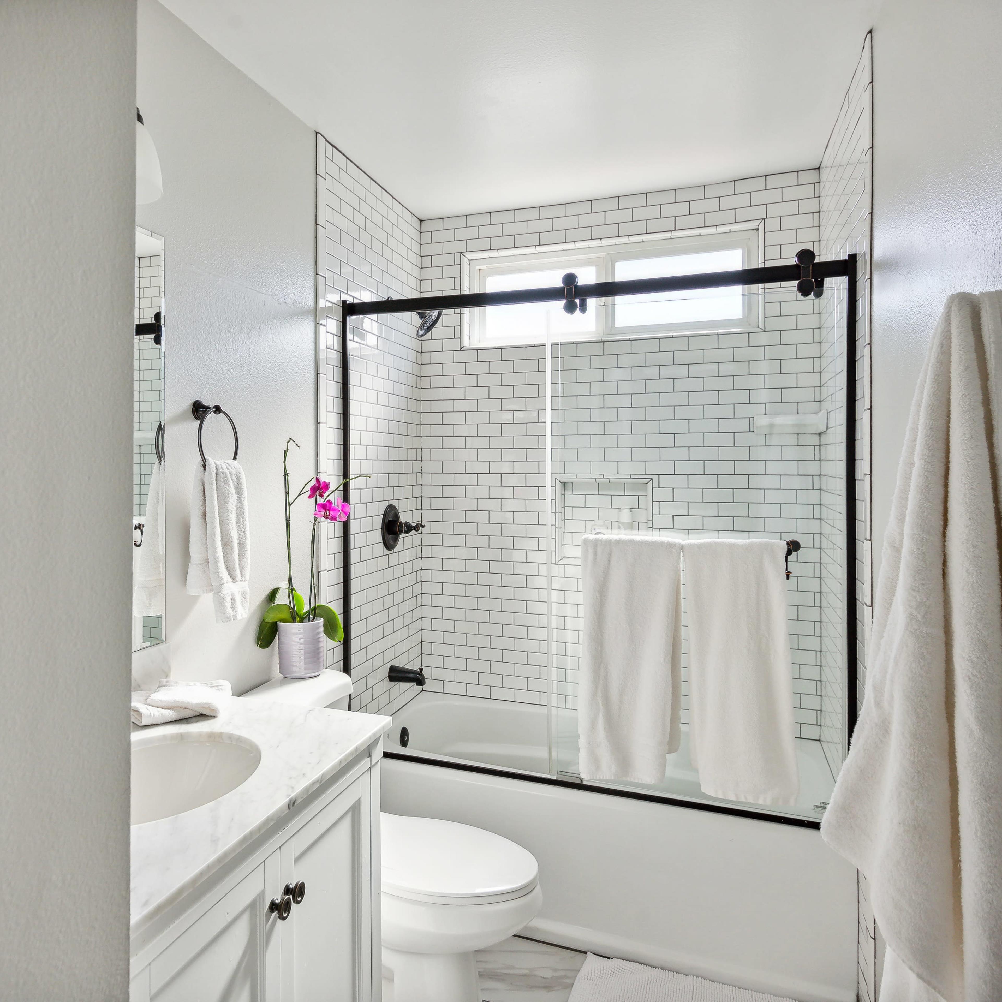A modern bathroom with a glass-enclosed shower, white subway tile walls, a sink with a cabinet, and towels hanging neatly.