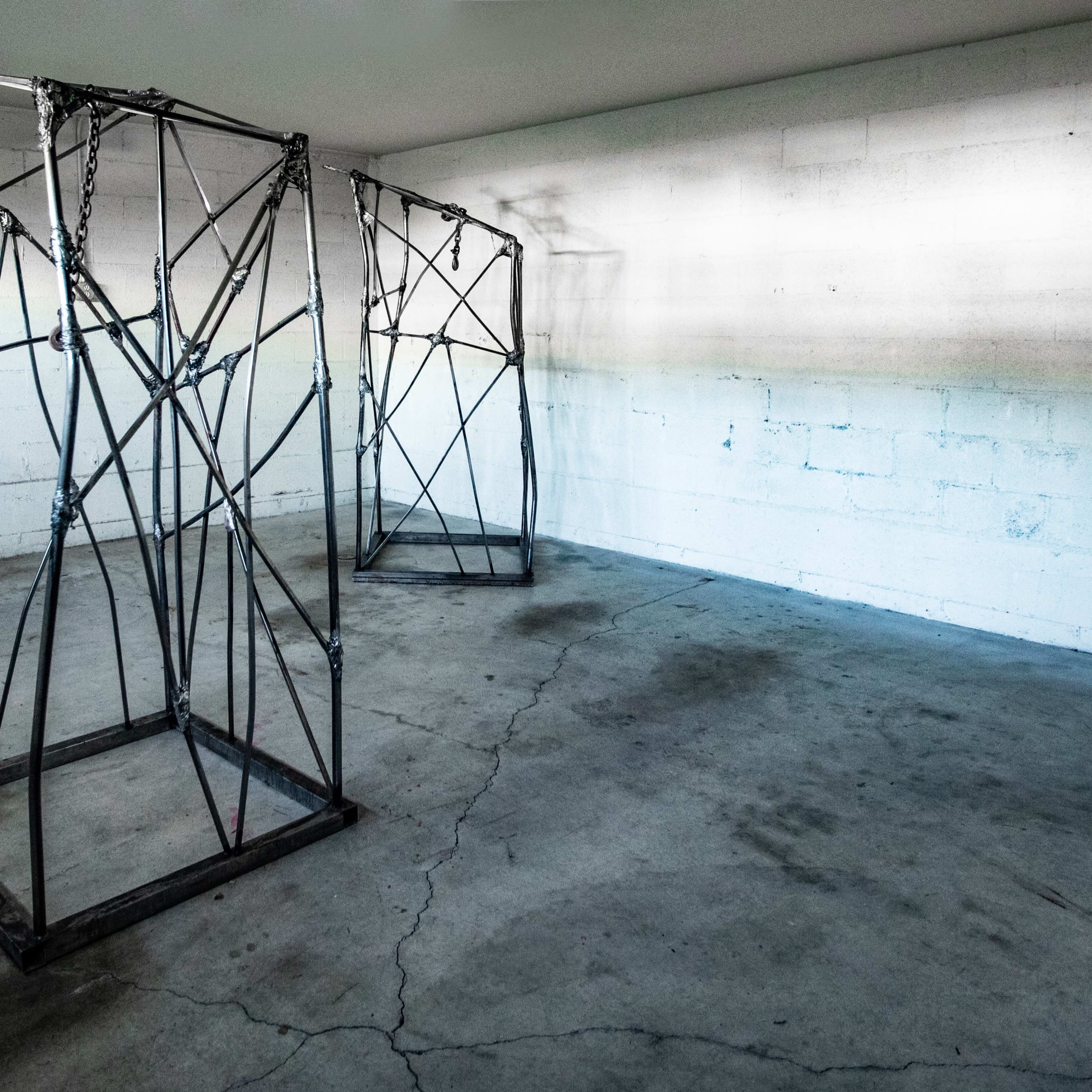 Two large metal frame structures positioned in an empty indoor space with a concrete floor and bare walls.