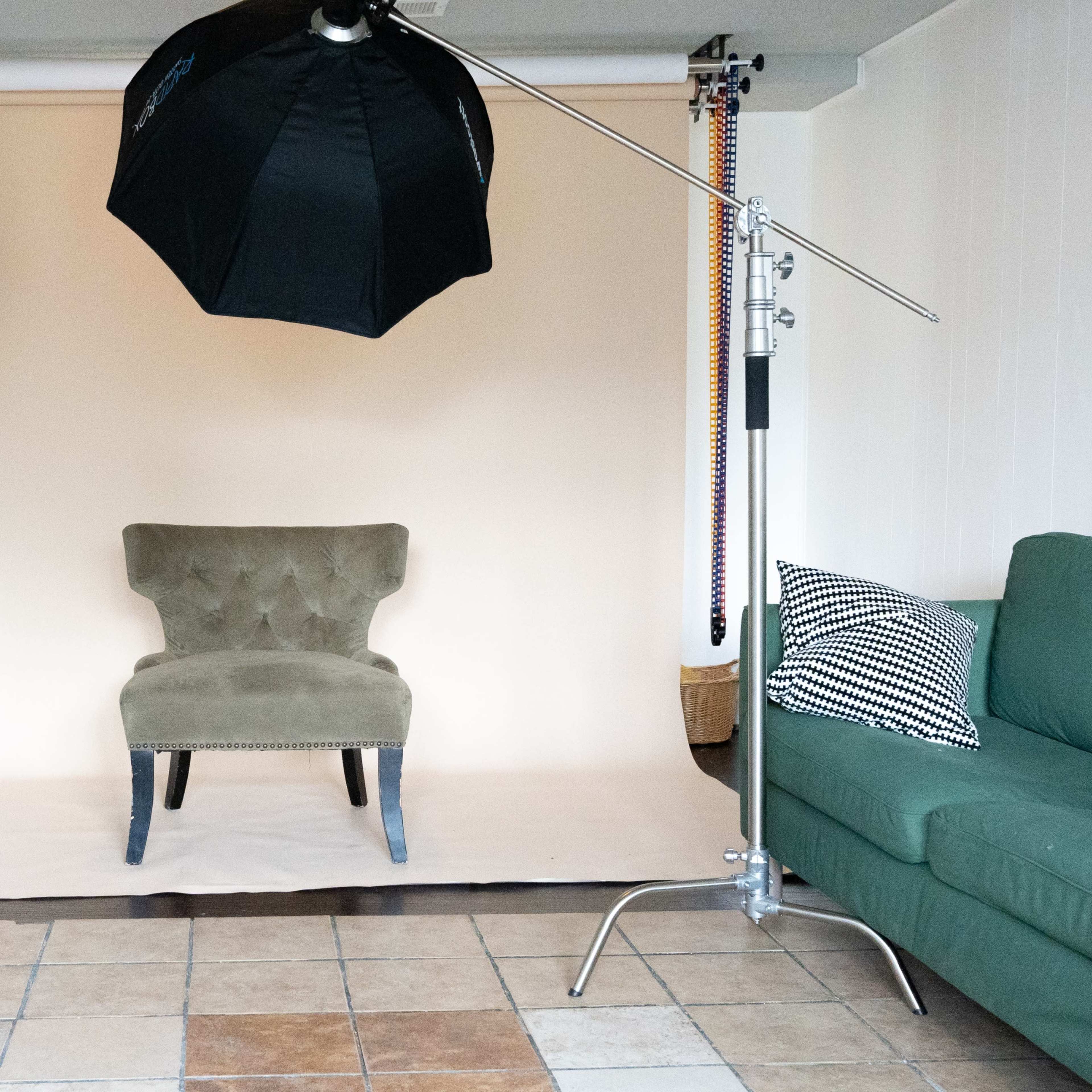 A photography studio setup with a single upholstered chair placed in front of a light-colored backdrop, accompanied by two softbox lights and a reflector.