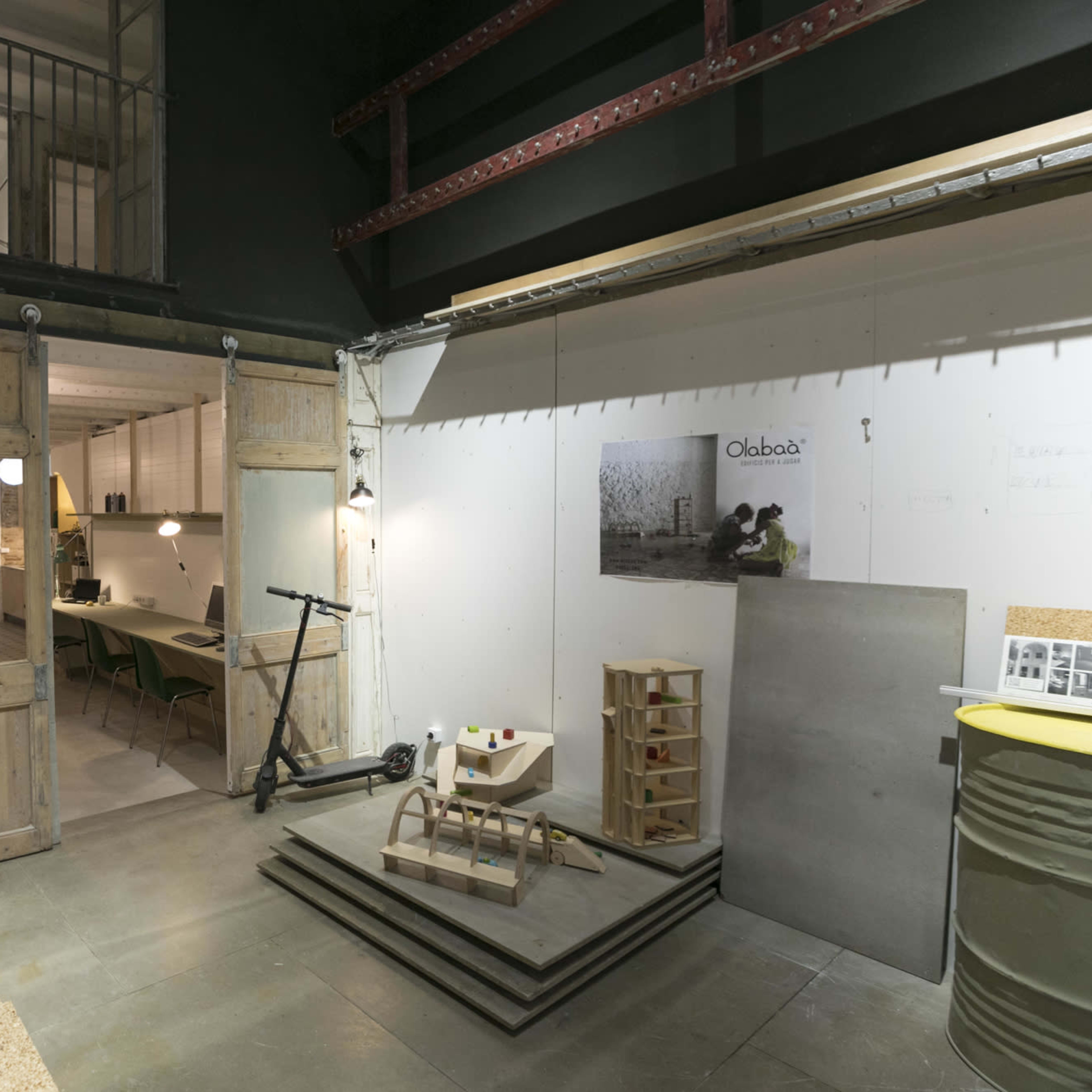 An interior space featuring wooden sliding doors, a scooter, and stacks of cork boards with tables and chairs in the background.