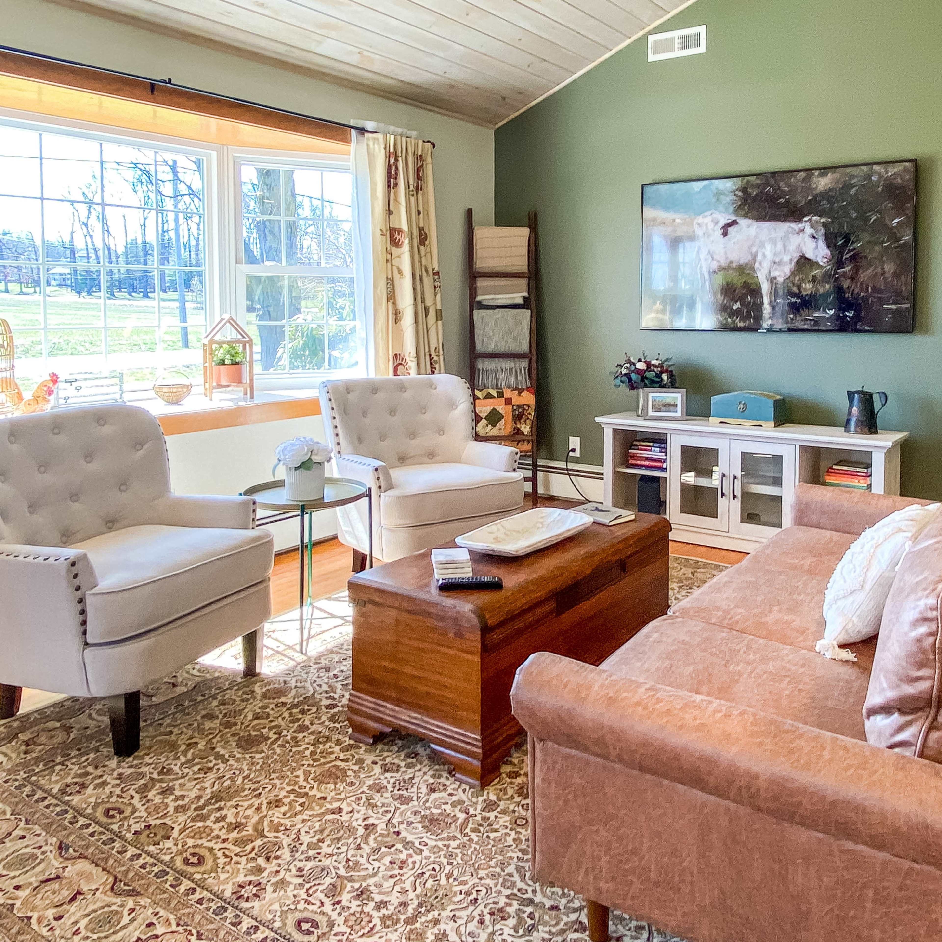 A living room with two armchairs, a coffee table, and a couch arranged around a large window that overlooks a green space.