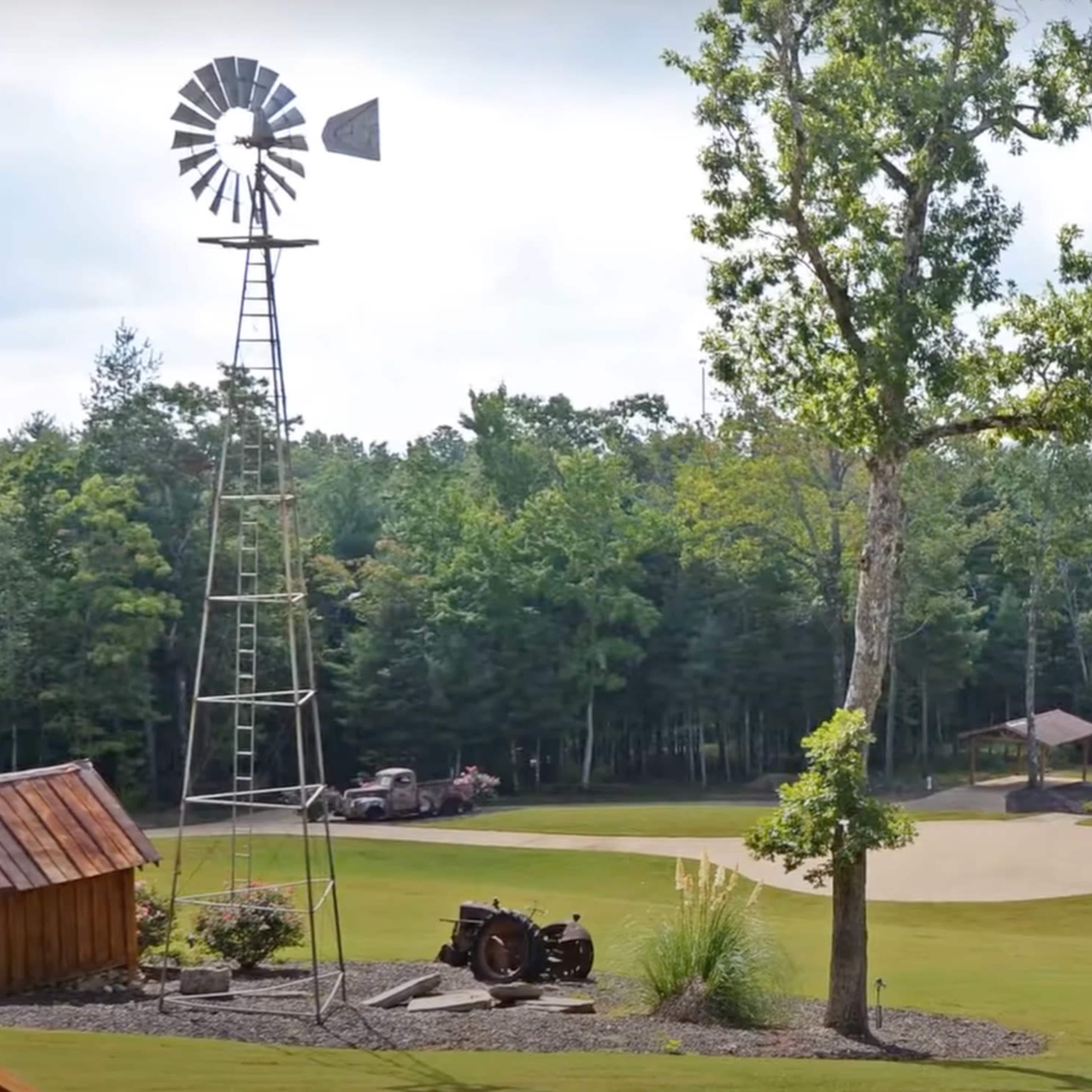 A large, wooded property featuring a windmill, a vintage tractor, and a spacious rustic-style lodge.