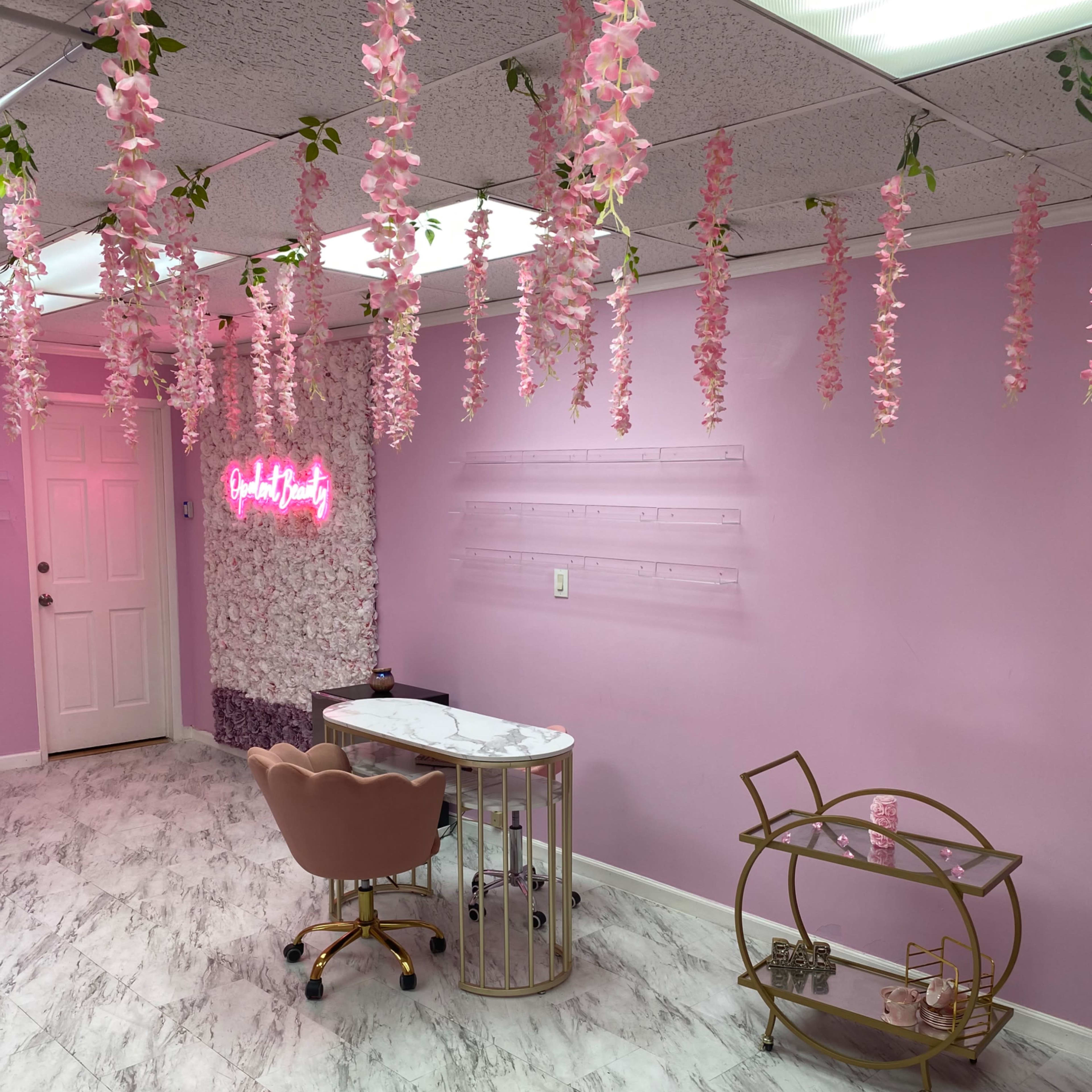 A salon interior with pink walls, a marble topped desk, a chair, and decorative faux flowers hanging from the ceiling.
