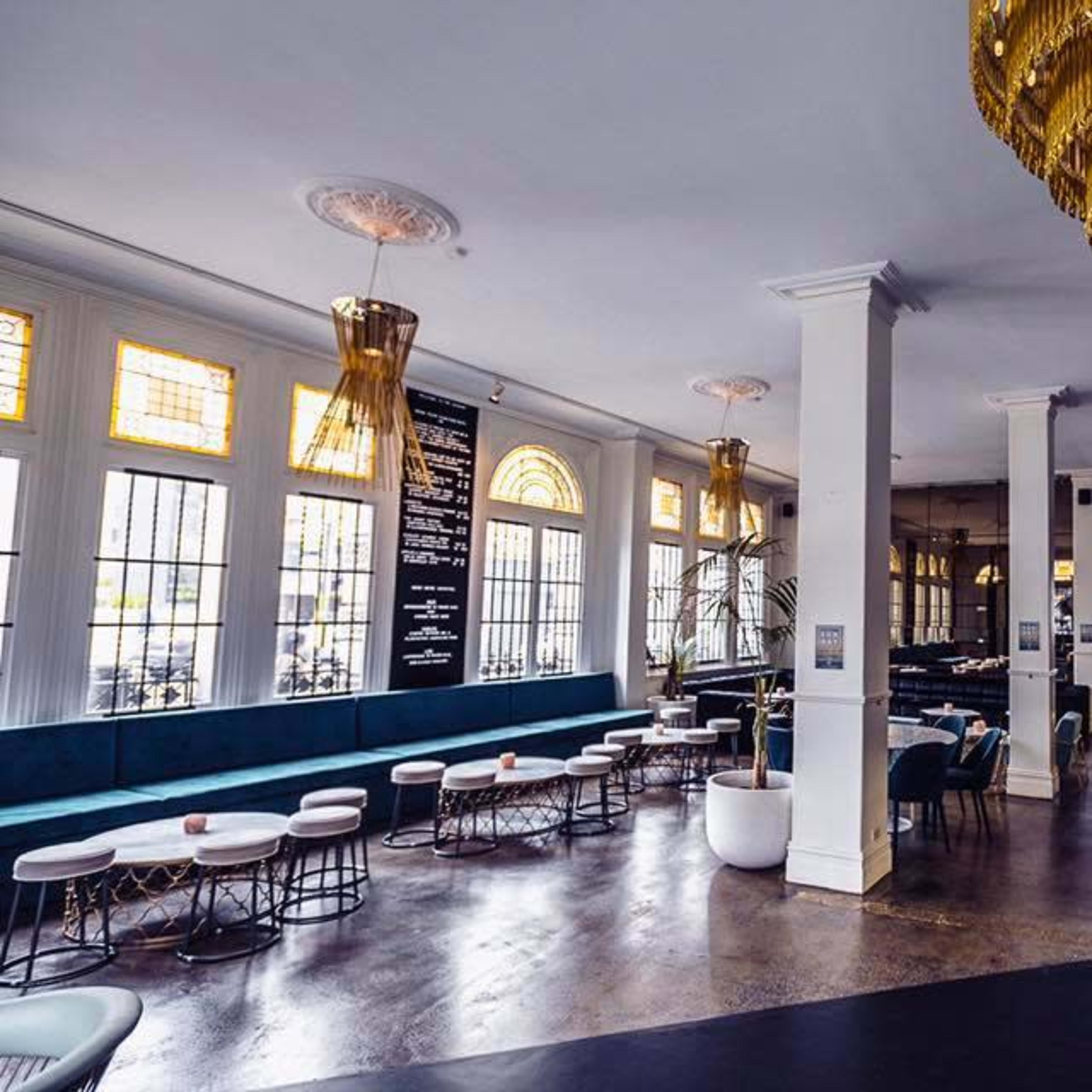A spacious bar and lounge area featuring a modern design with golden chandeliers, plush seating, and a sleek bar counter.