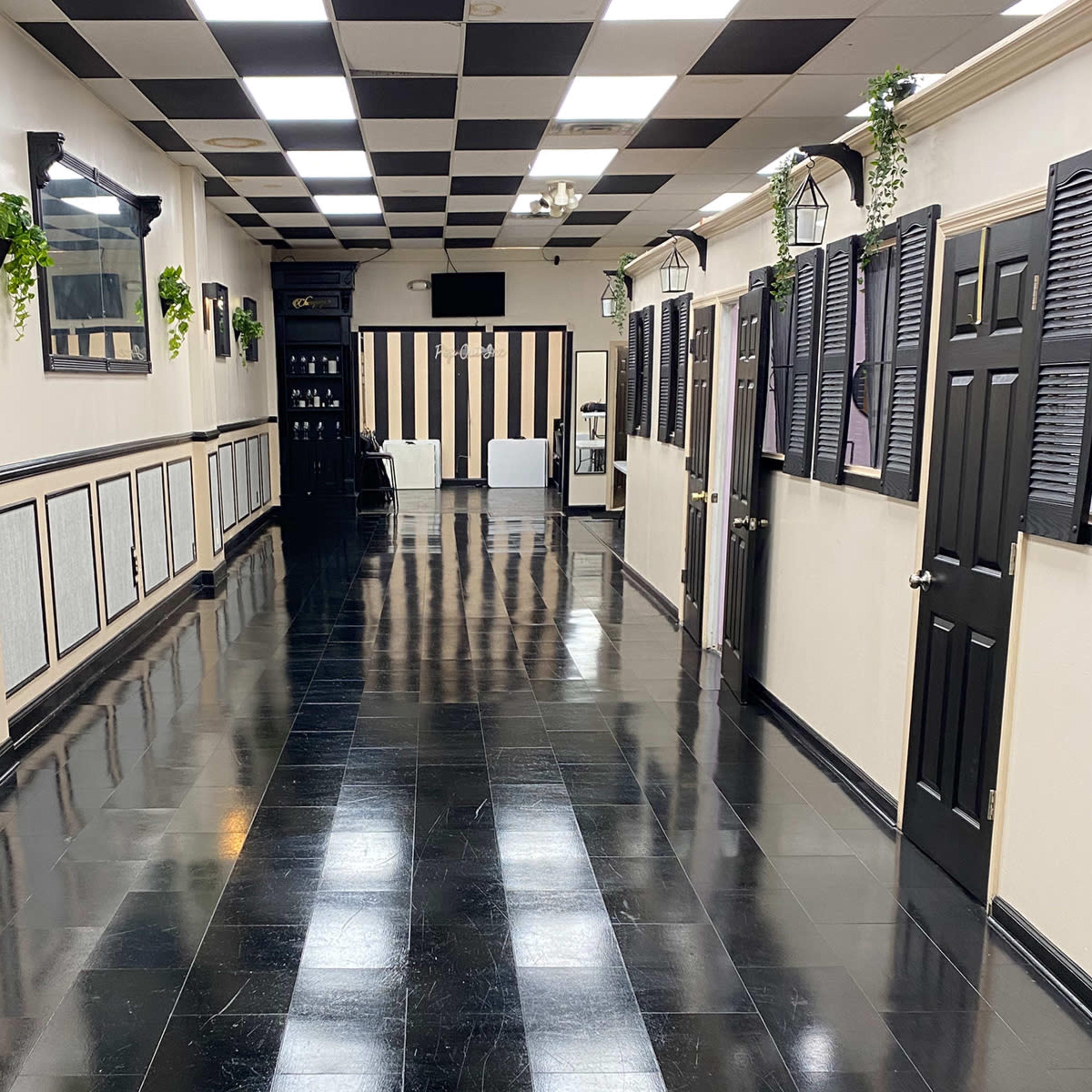 A long, narrow hallway with black and white checkered tiles, flanked by doors and wall decorations, leading to a seating area at the far end.
