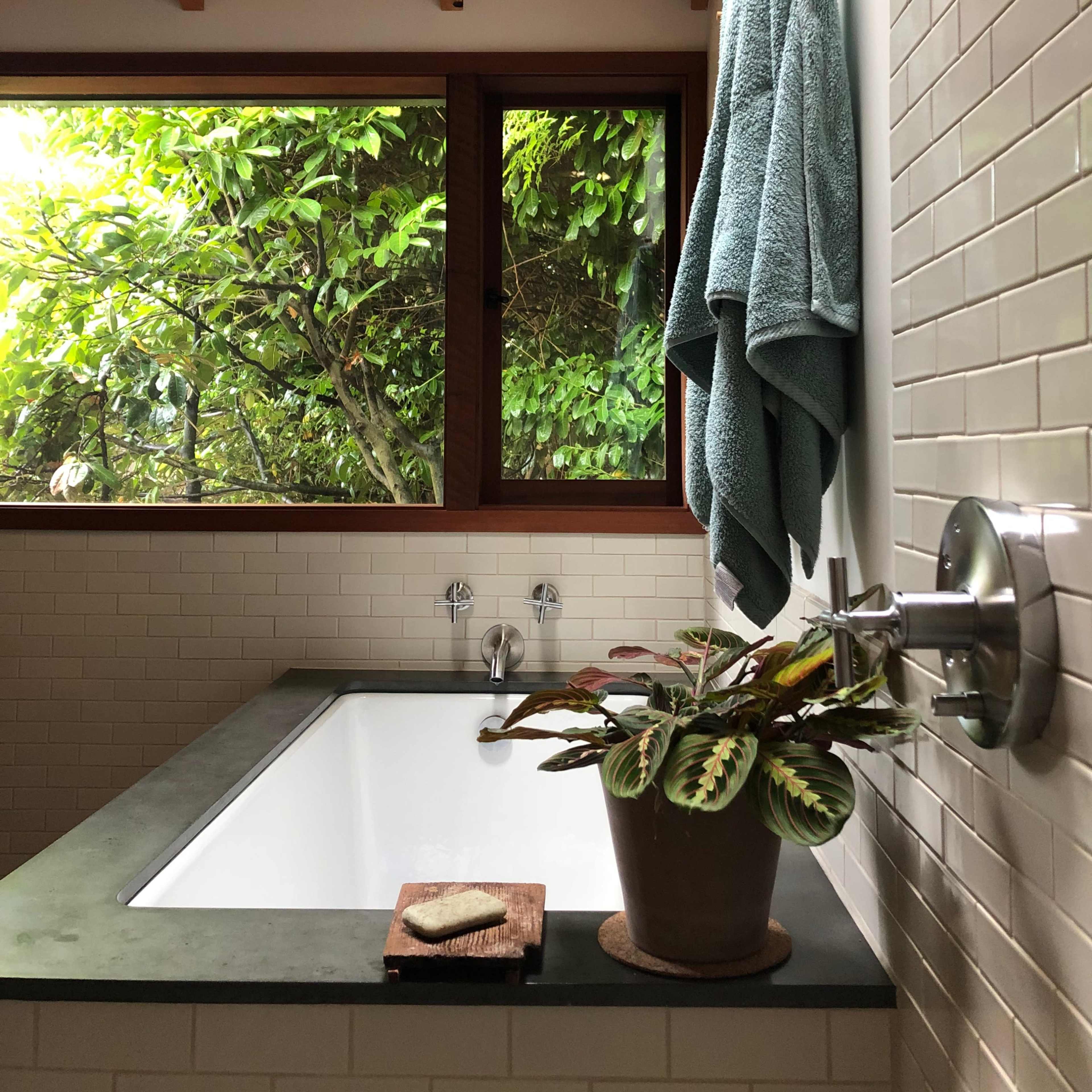 A modern bathroom features a tub next to a large window with lush greenery outside.