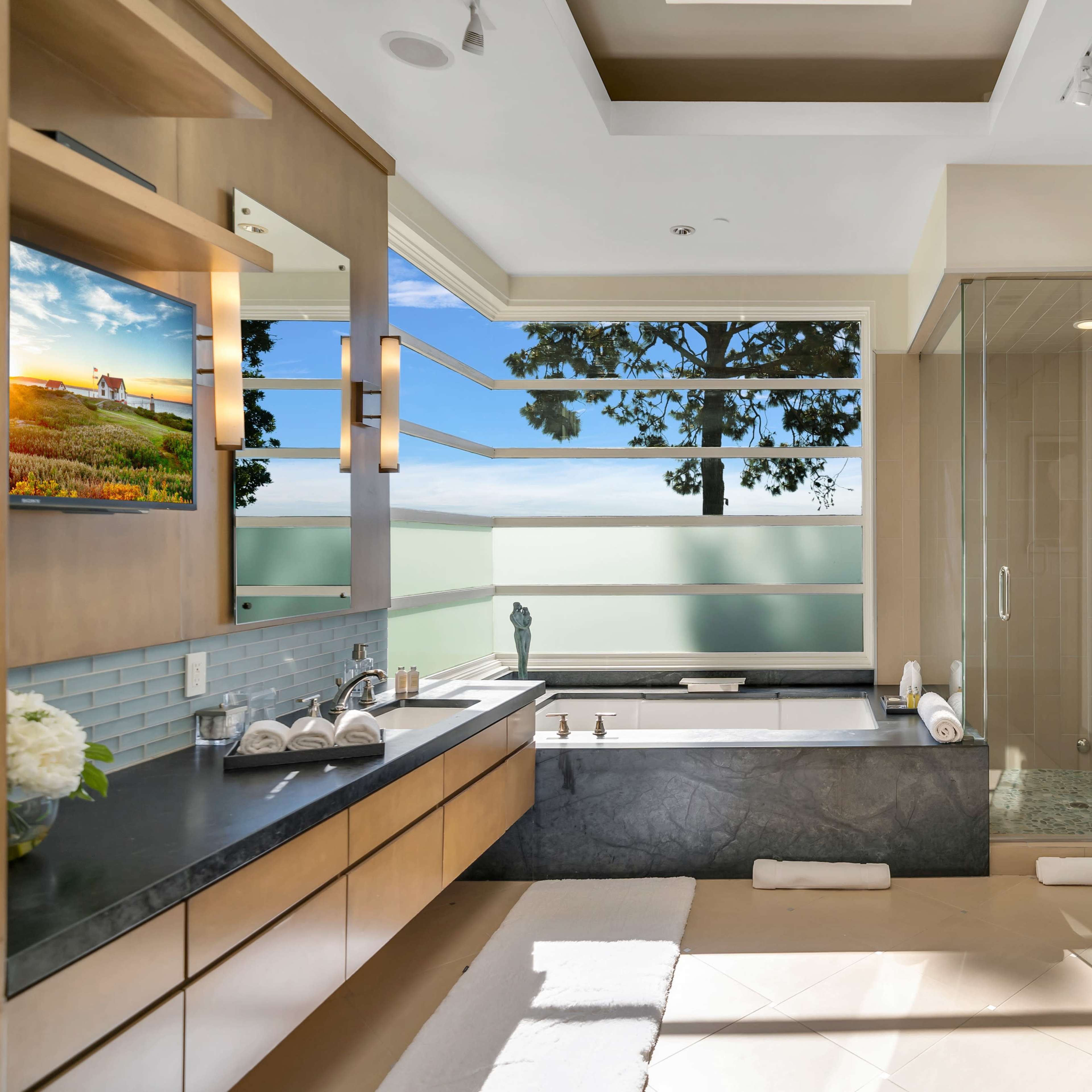 A modern bathroom features a soaking tub, a glass-enclosed shower, and large windows offering a view of the outdoors.