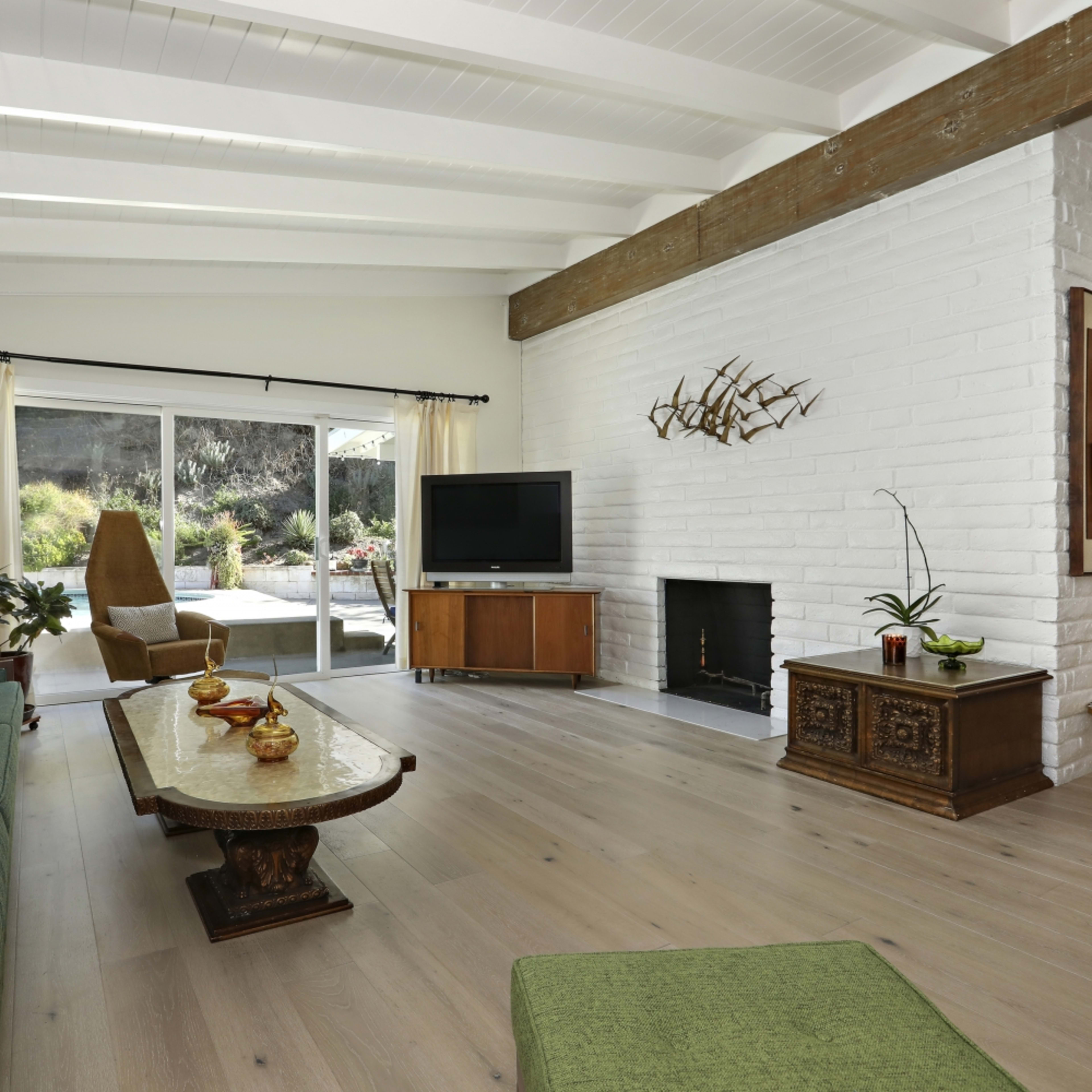 The living room features a spacious layout with a light color palette, a large window, a fireplace, and modern furniture.