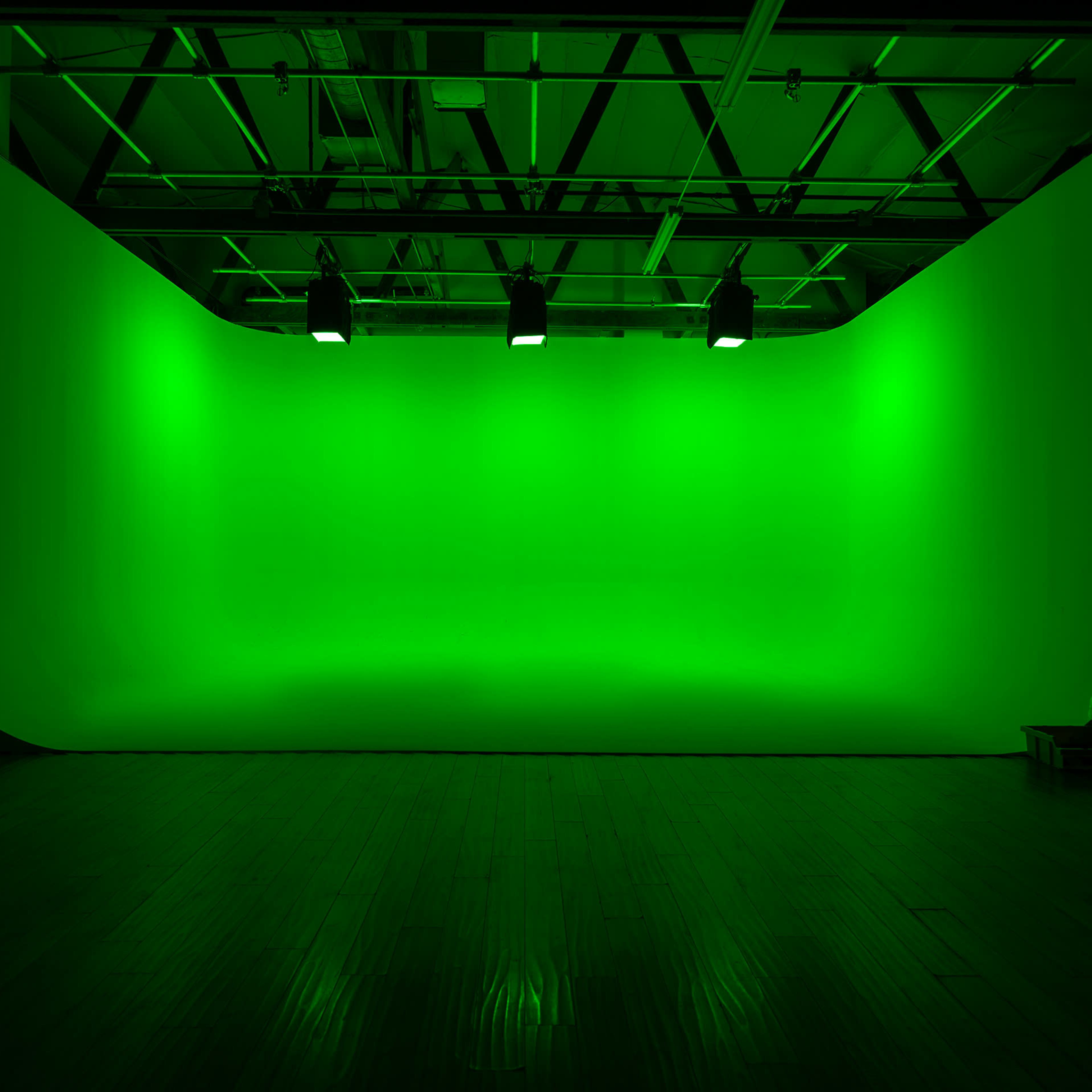 A studio space features a large green backdrop illuminated by overhead lights.