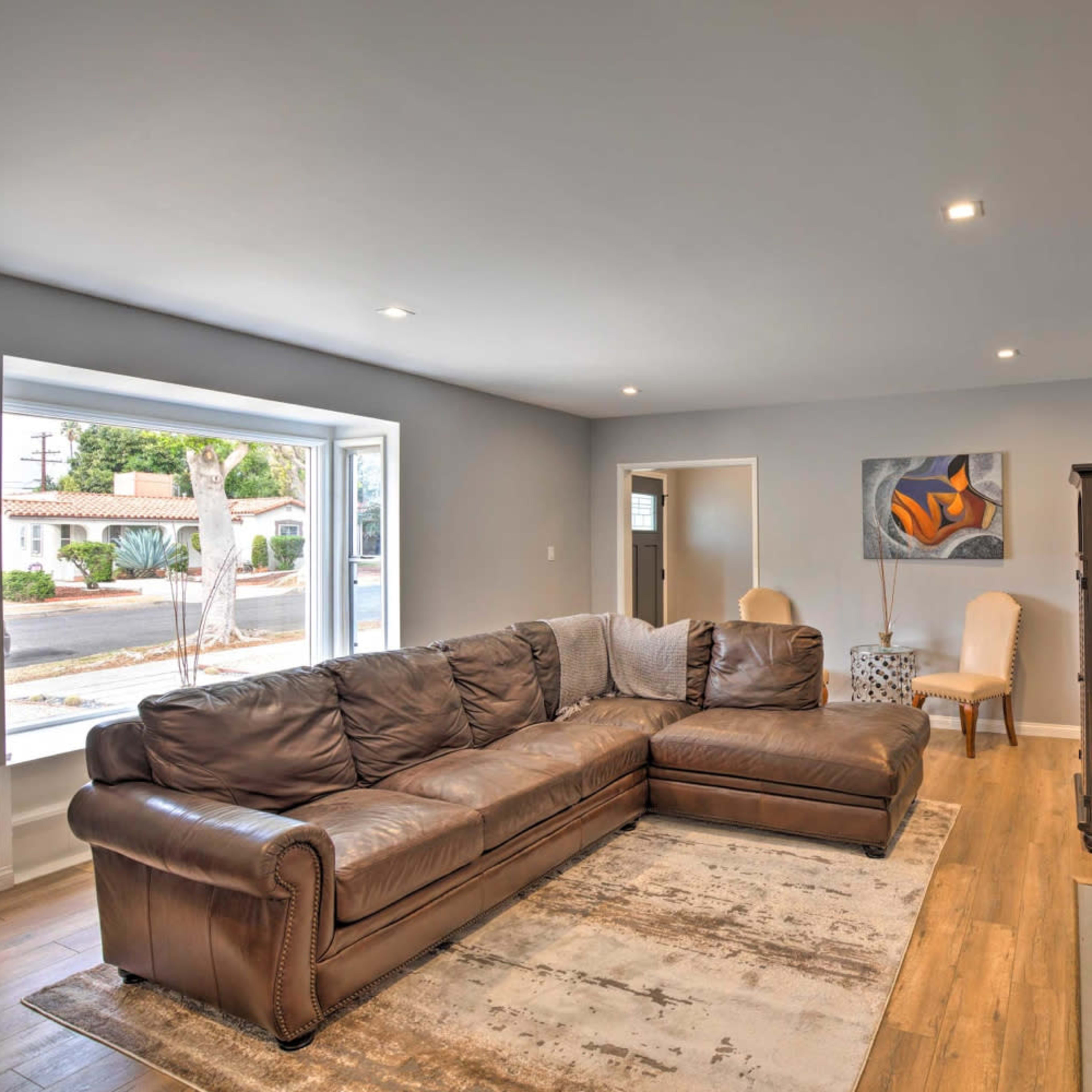 A modern living room with a large brown sectional sofa, a fireplace, and a window facing the street.