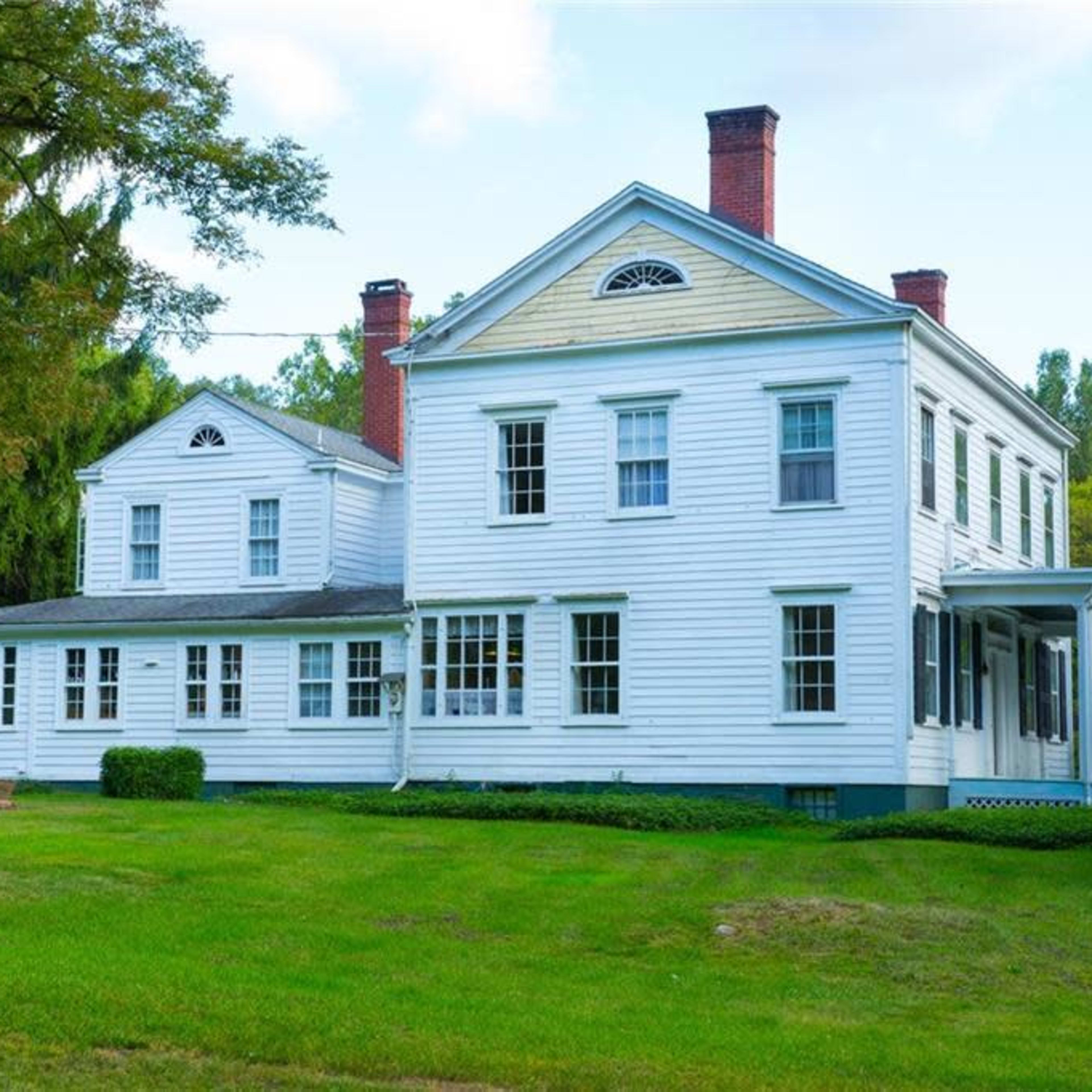 A two-story white colonial-style house with a large front porch and well-maintained lawn.