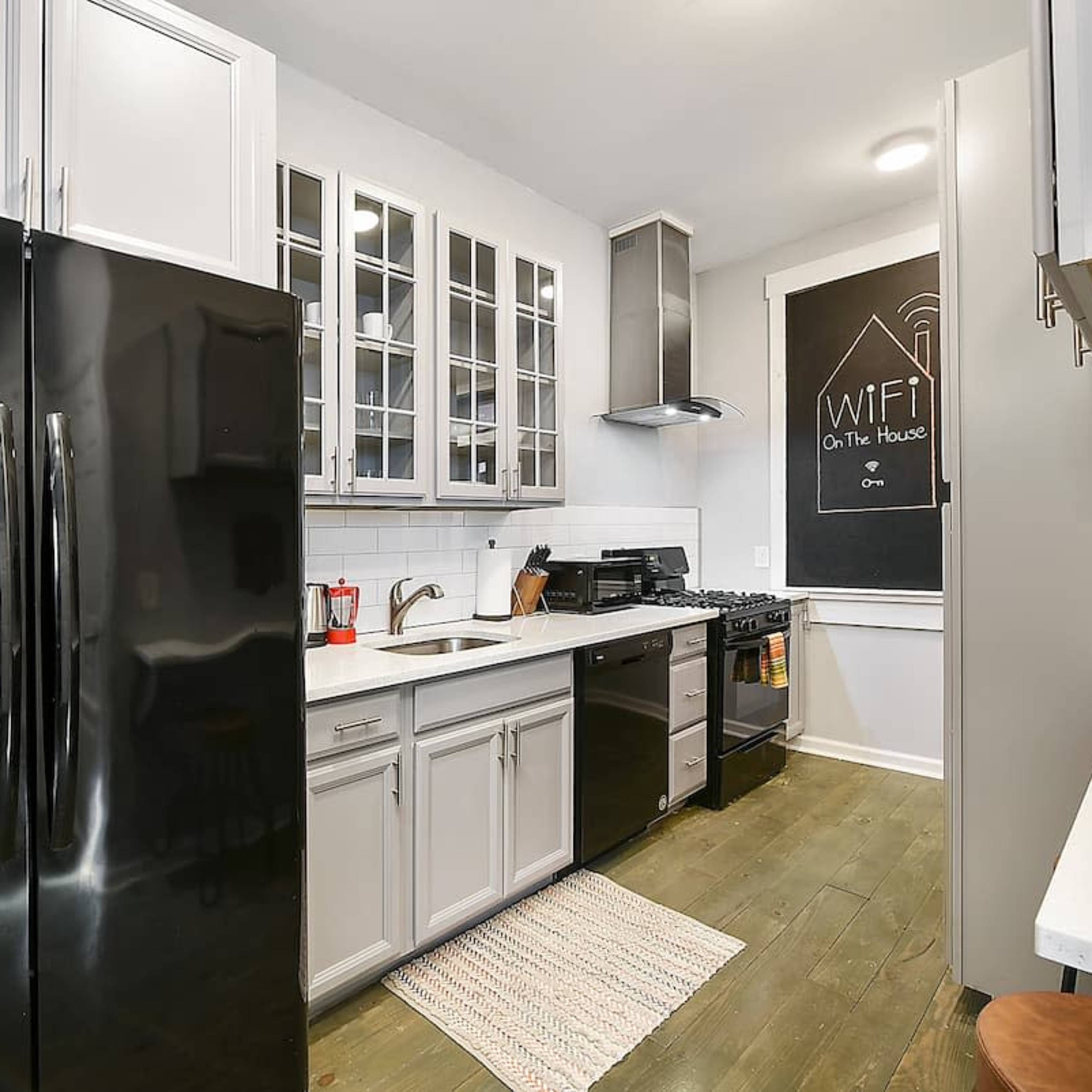 A modern kitchen features black appliances, white cabinetry, and a chalkboard wall listing WiFi details.