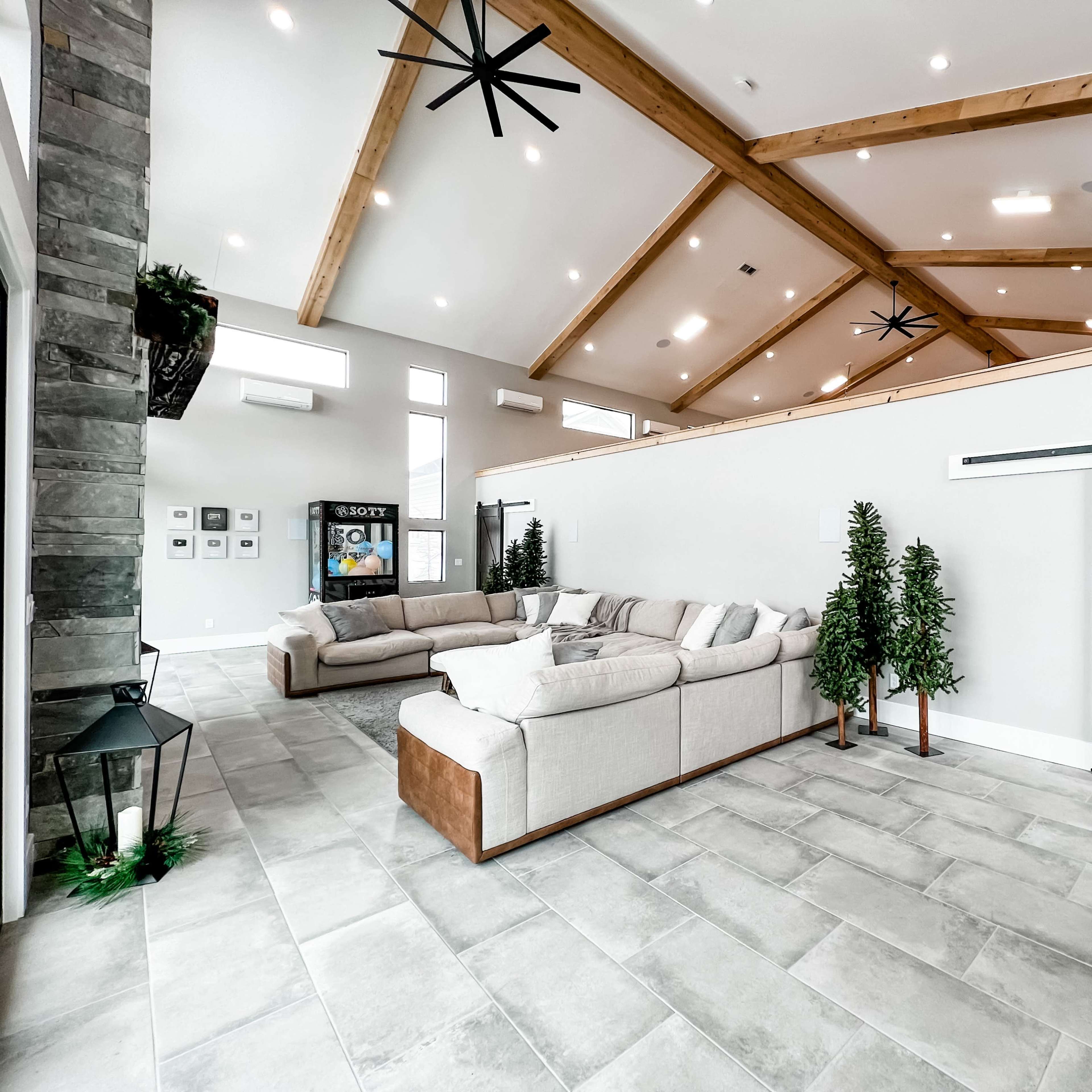 The spacious living area features a high ceiling with wooden beams, modern furniture, and large windows.