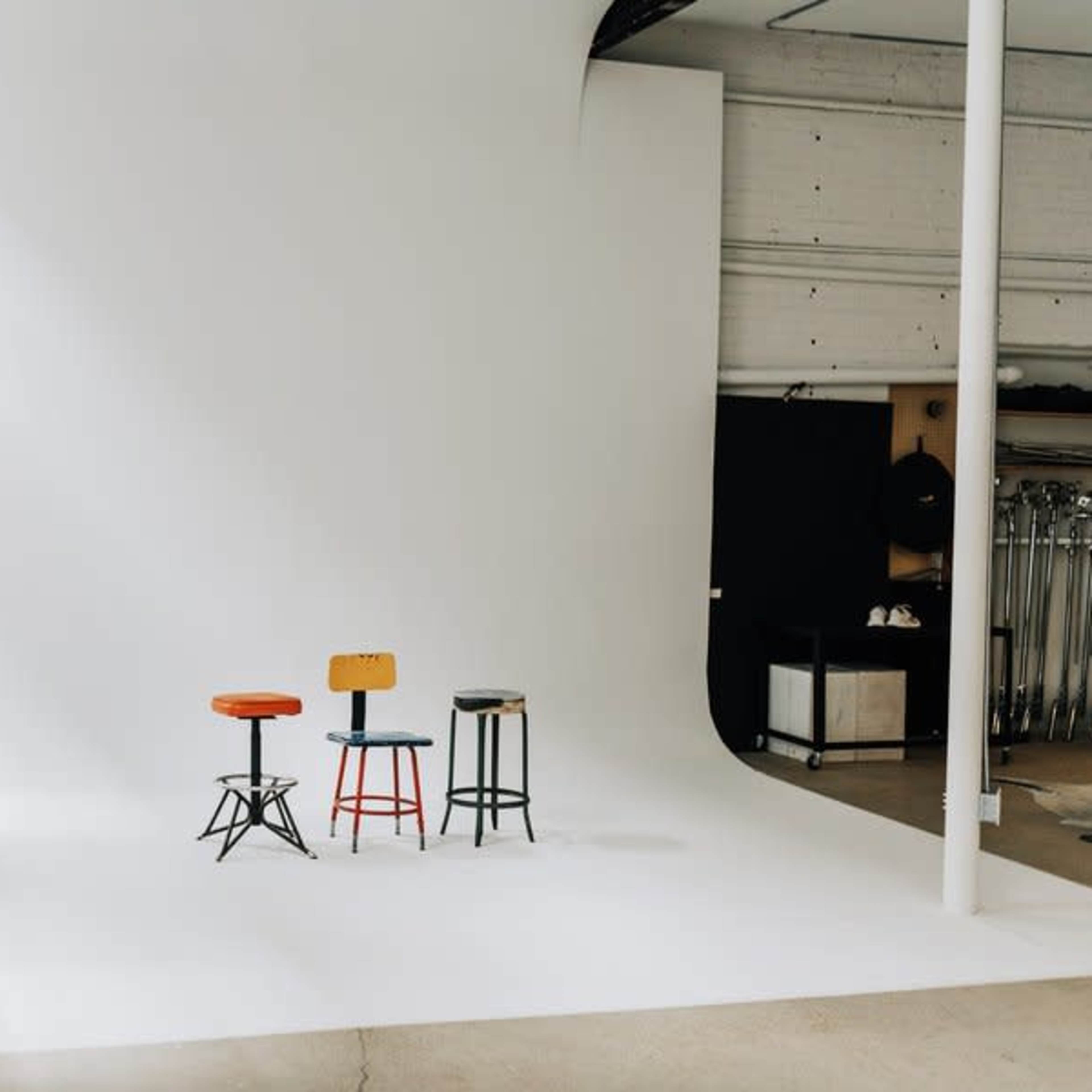 Three stools in red, orange, and green are positioned on a stark, white backdrop in a studio setting.