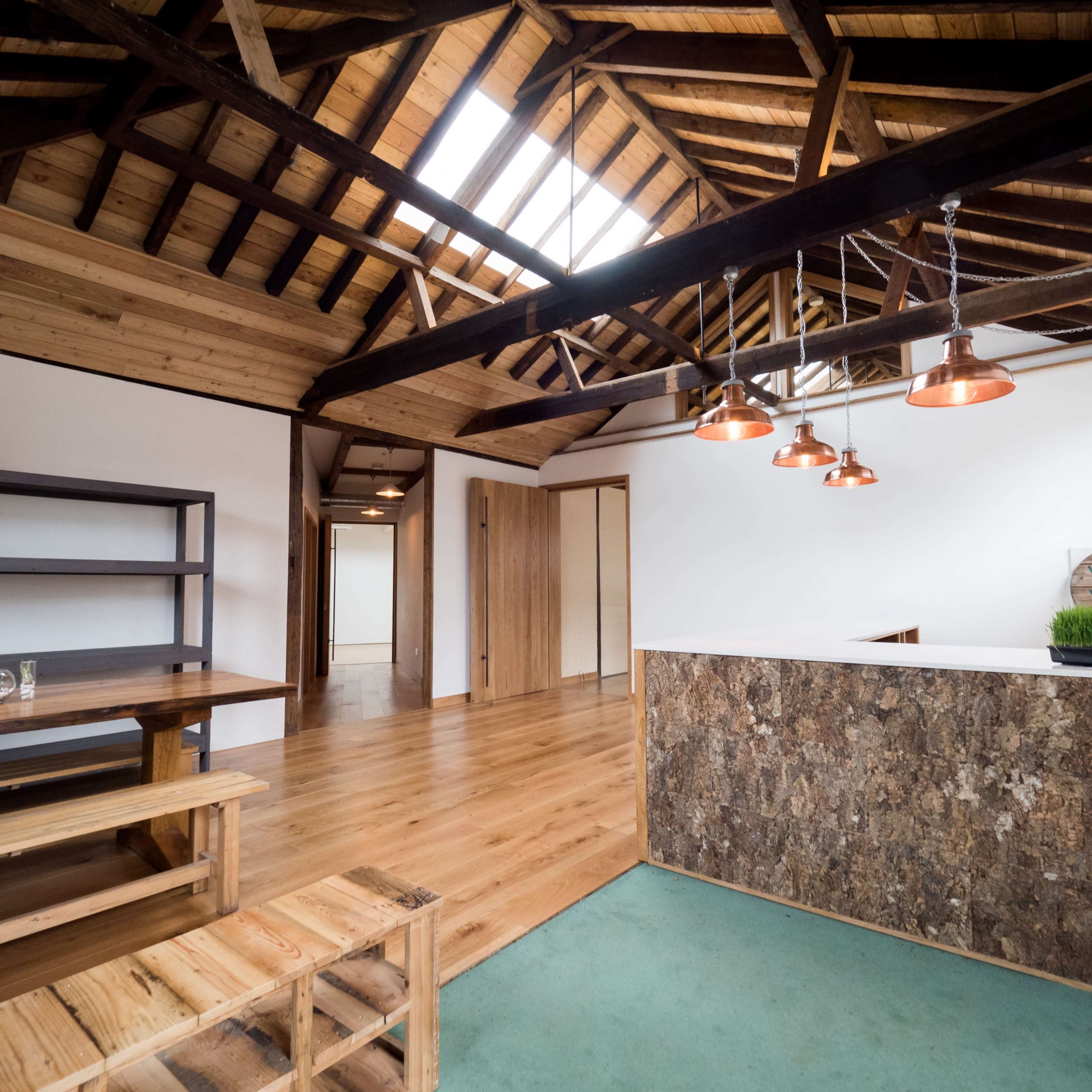 A spacious interior with wooden beams, a large open area featuring a dining table, and a counter with pendant lights.