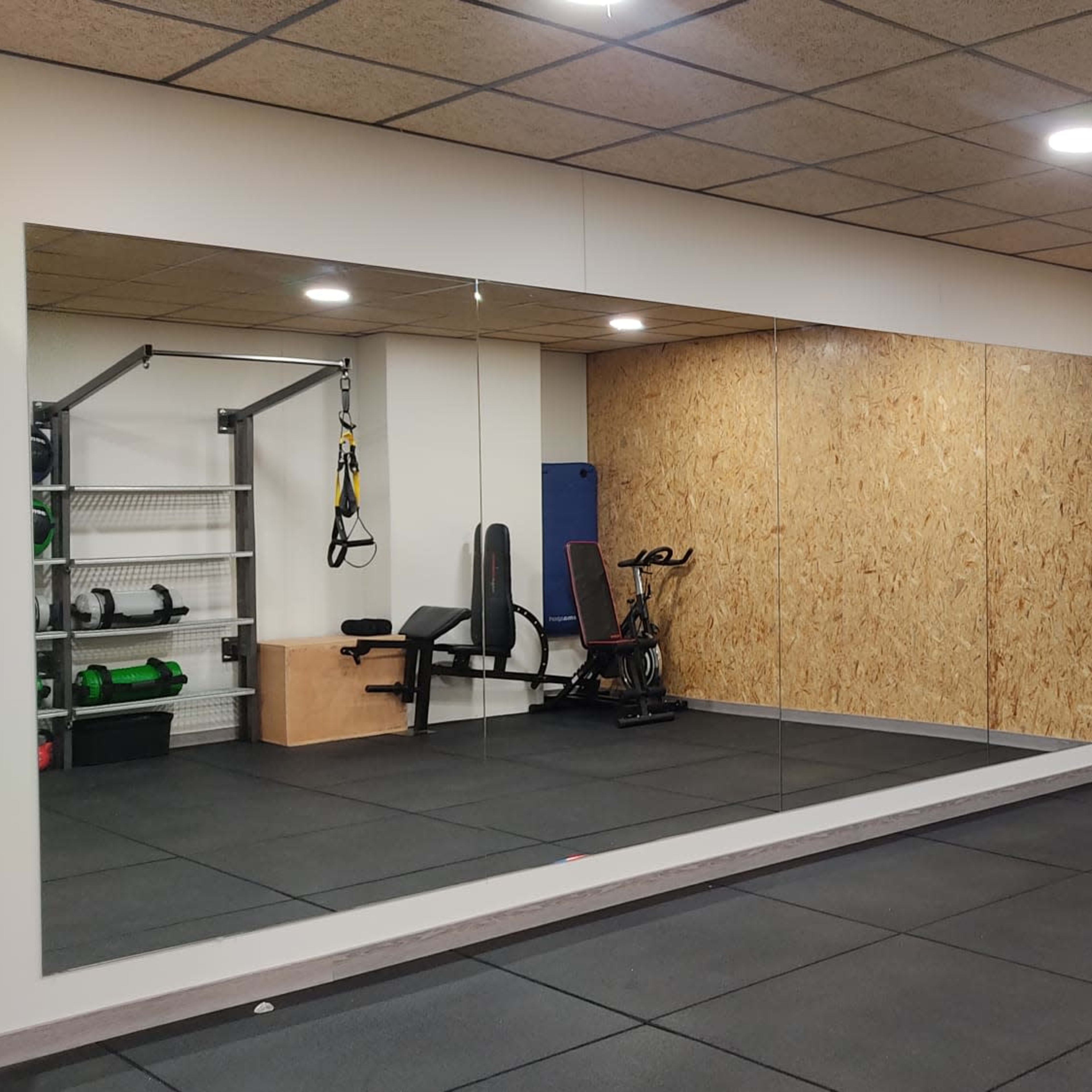 A gym space with a mirrored wall, workout equipment, and suspension training straps hanging from the ceiling.
