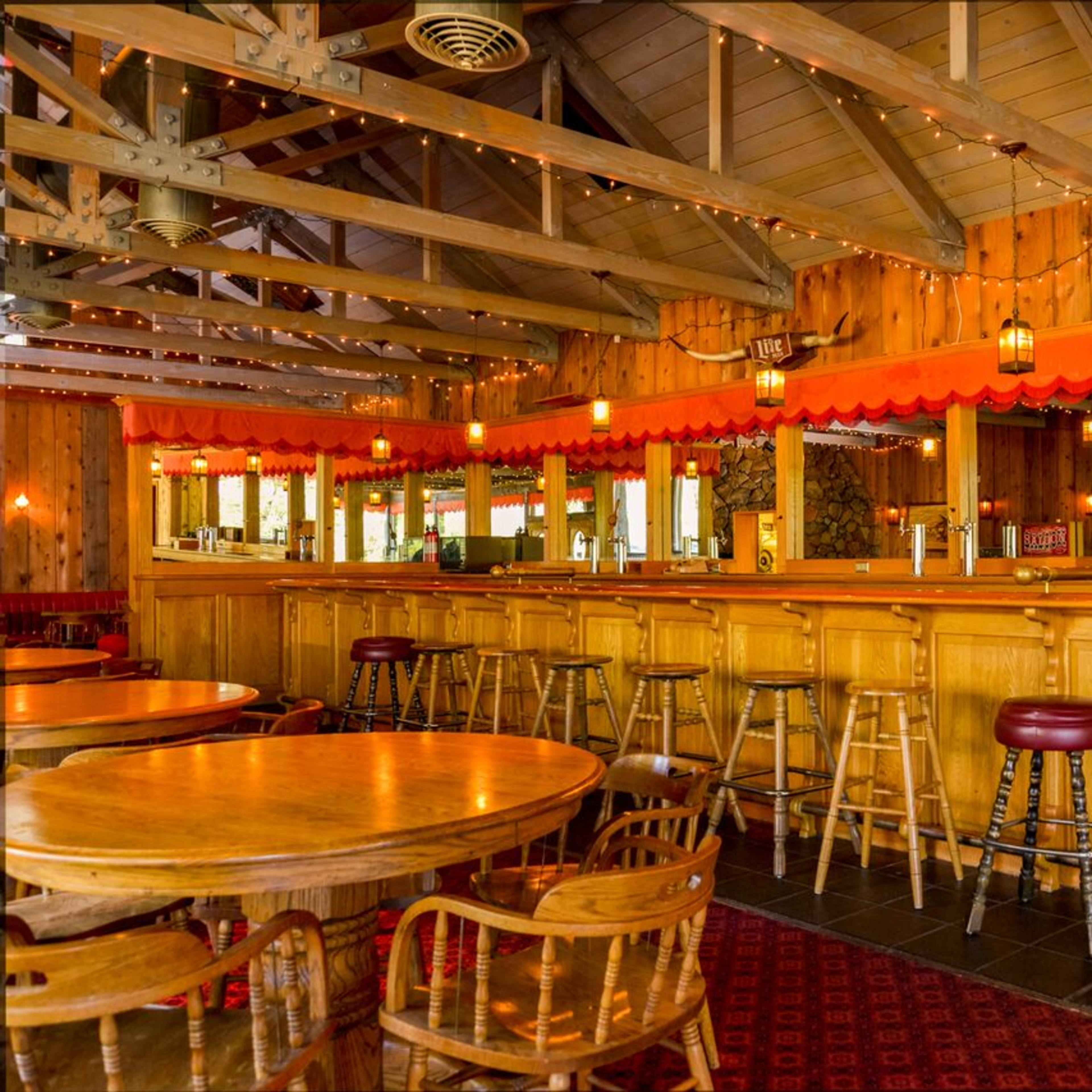 A wooden bar area with stools and tables, featuring warm lighting and rustic decor.