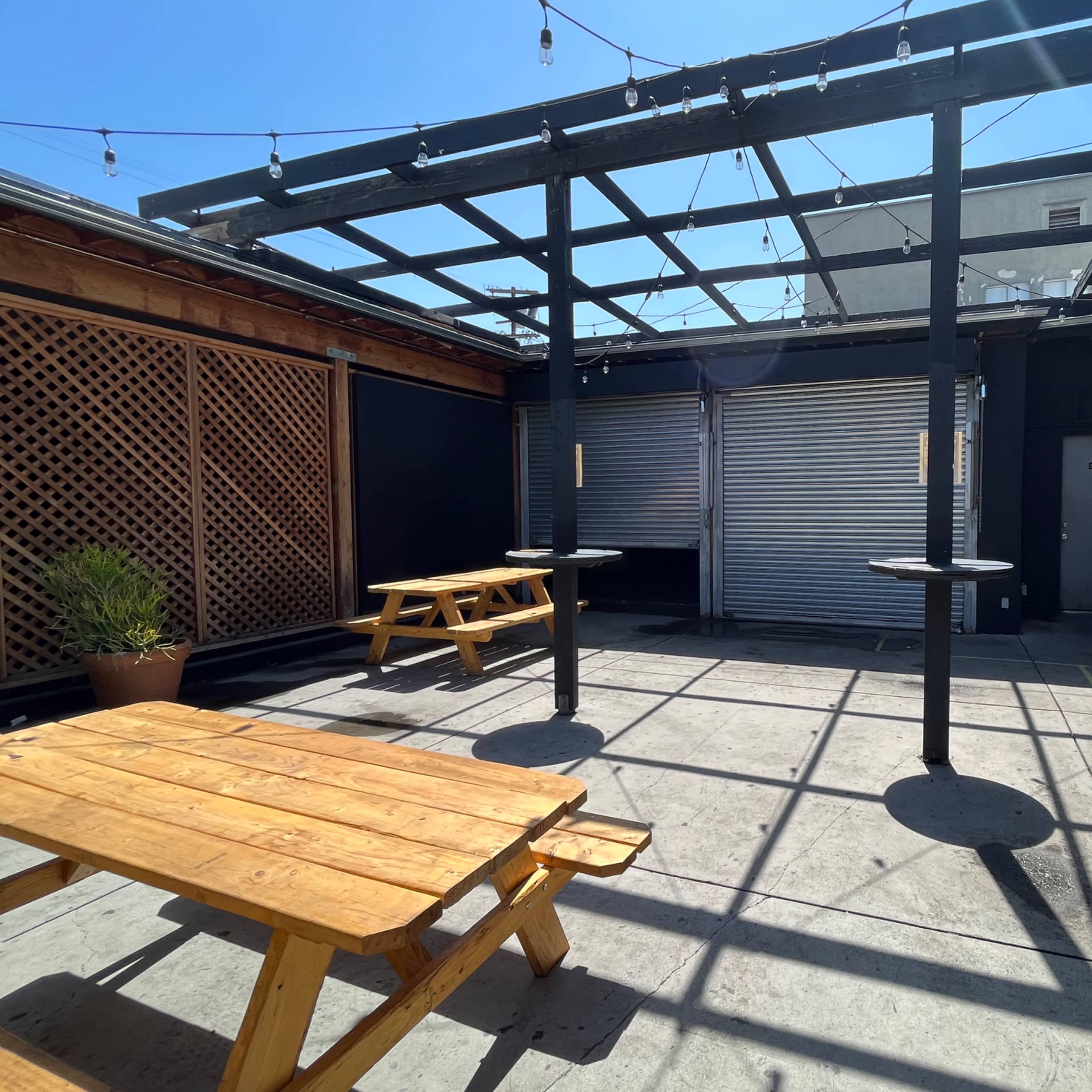 An empty outdoor patio with wooden benches, a striped awning, and overhead string lights.
