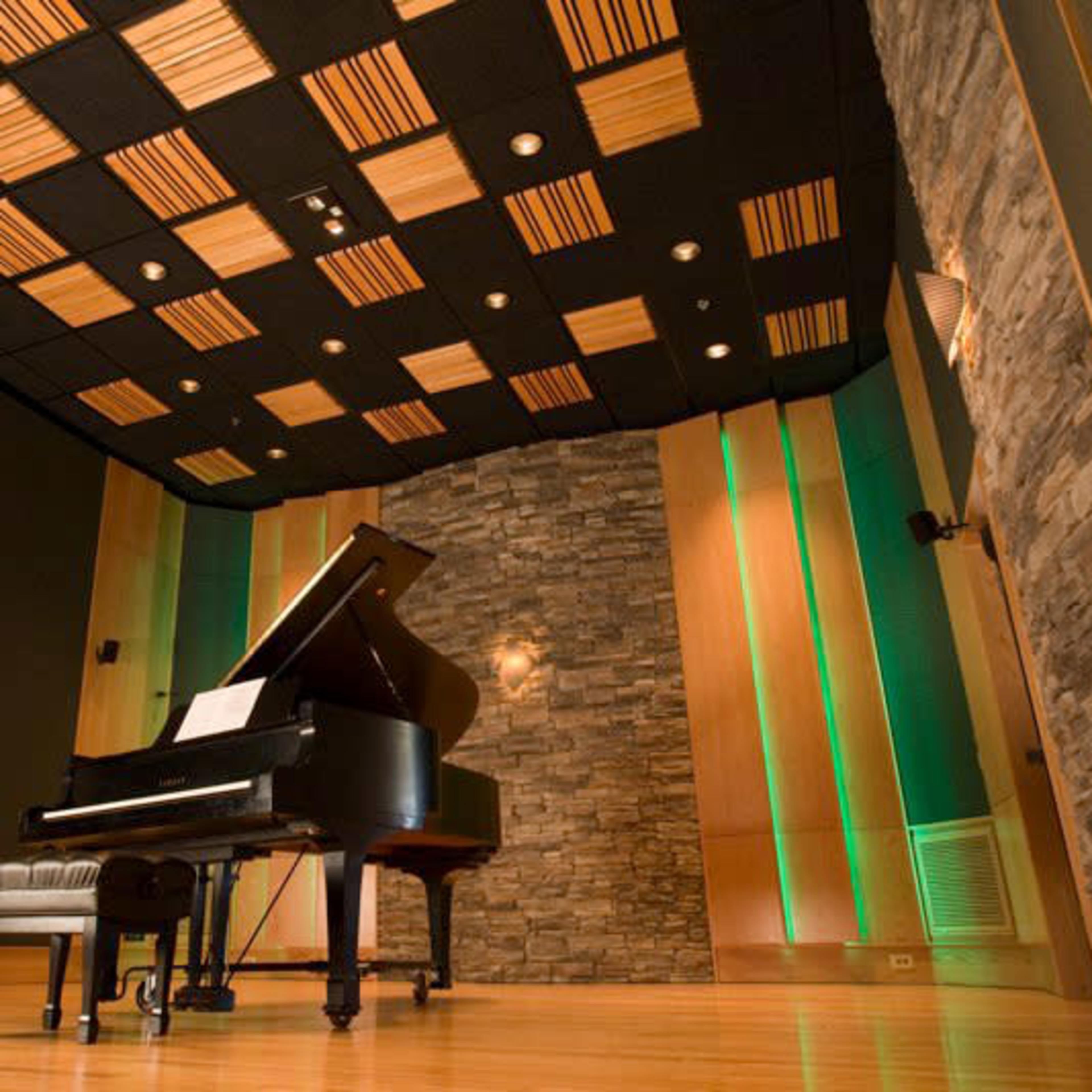 A grand piano positioned in a soundproof room with stone walls and wooden ceiling tiles.