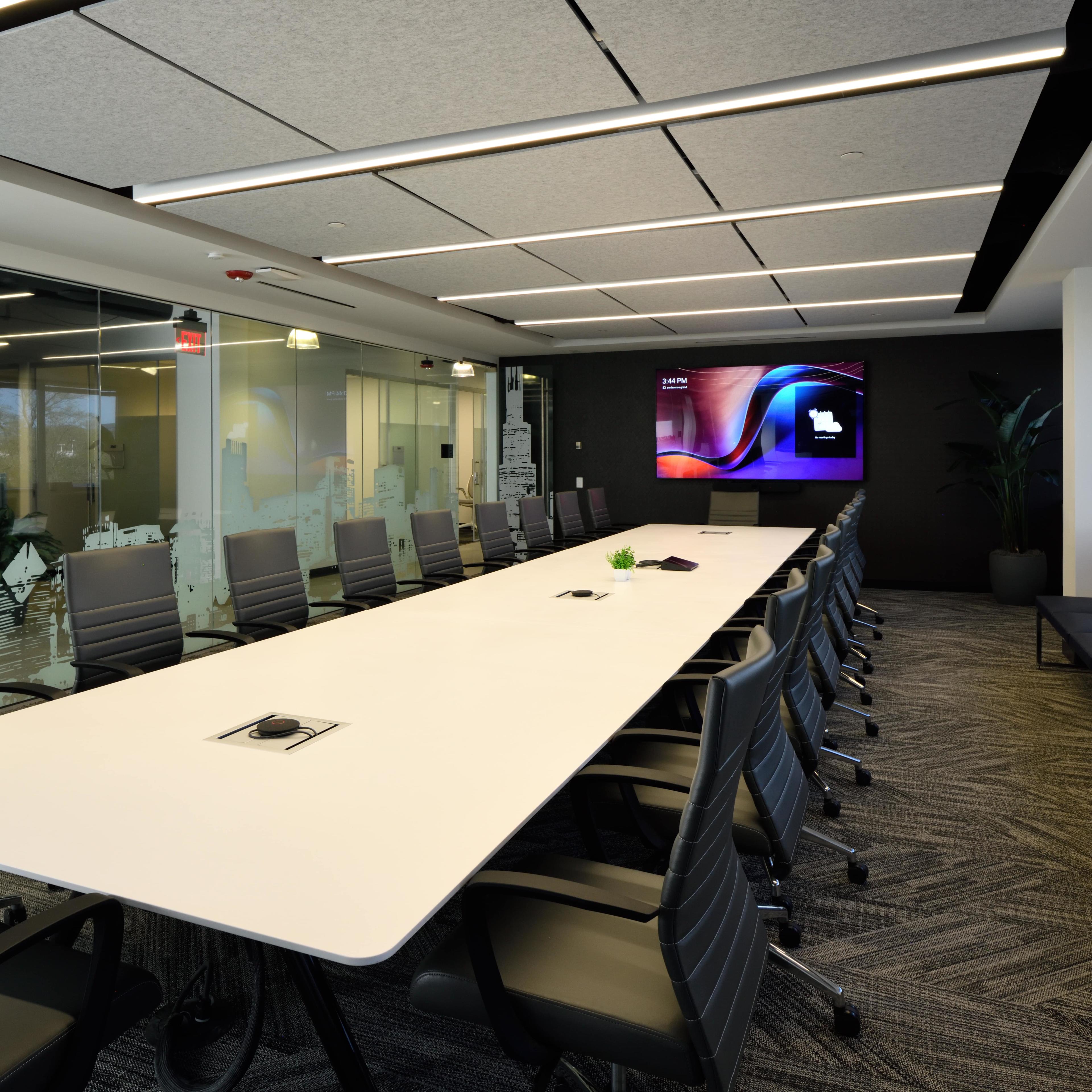 A modern conference room features a long white table surrounded by ergonomic chairs, with a large screen mounted on the wall and glass panels adorned with cityscape graphics.