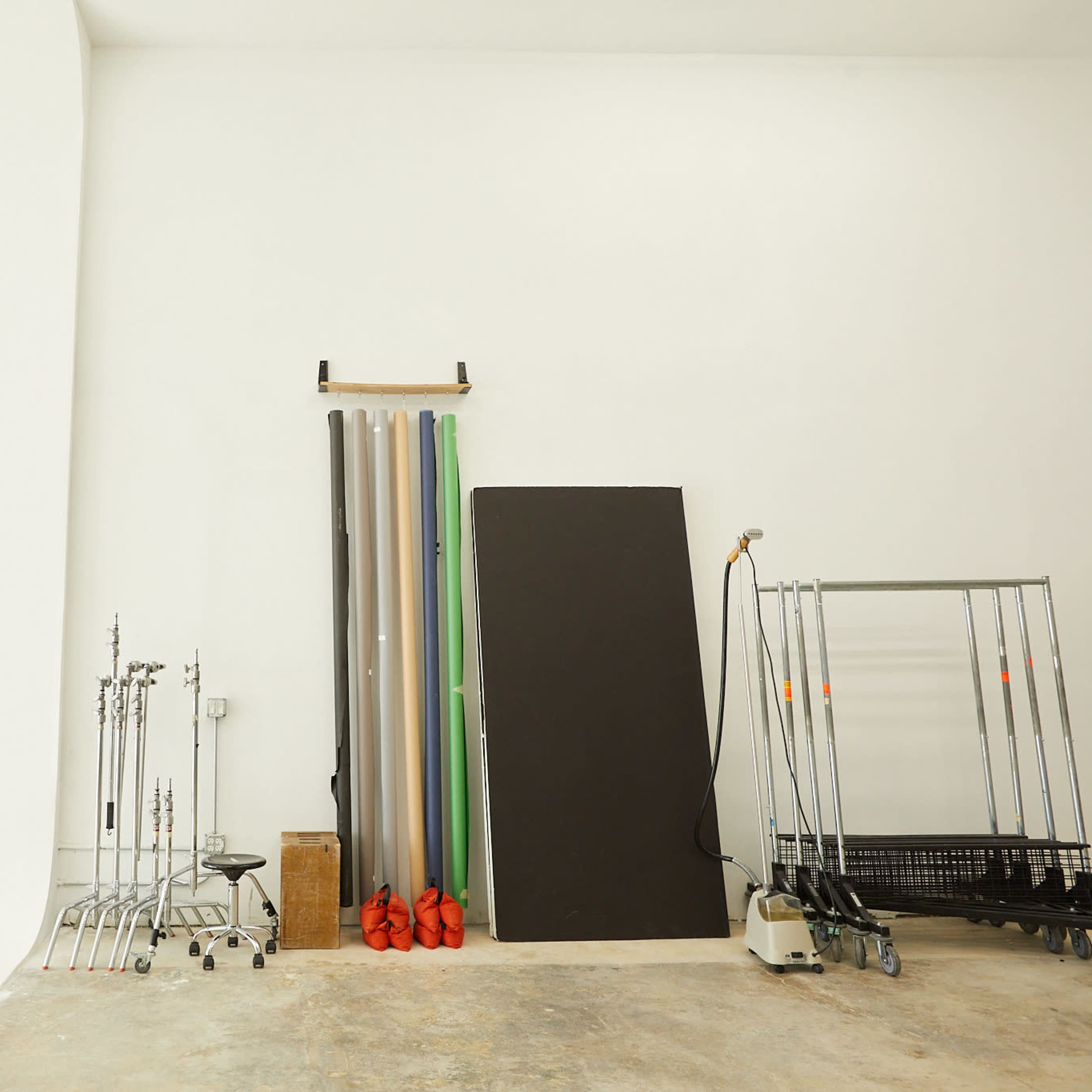 A photography studio with a seamless backdrop, various stands, and rolls of colored paper against a white wall.