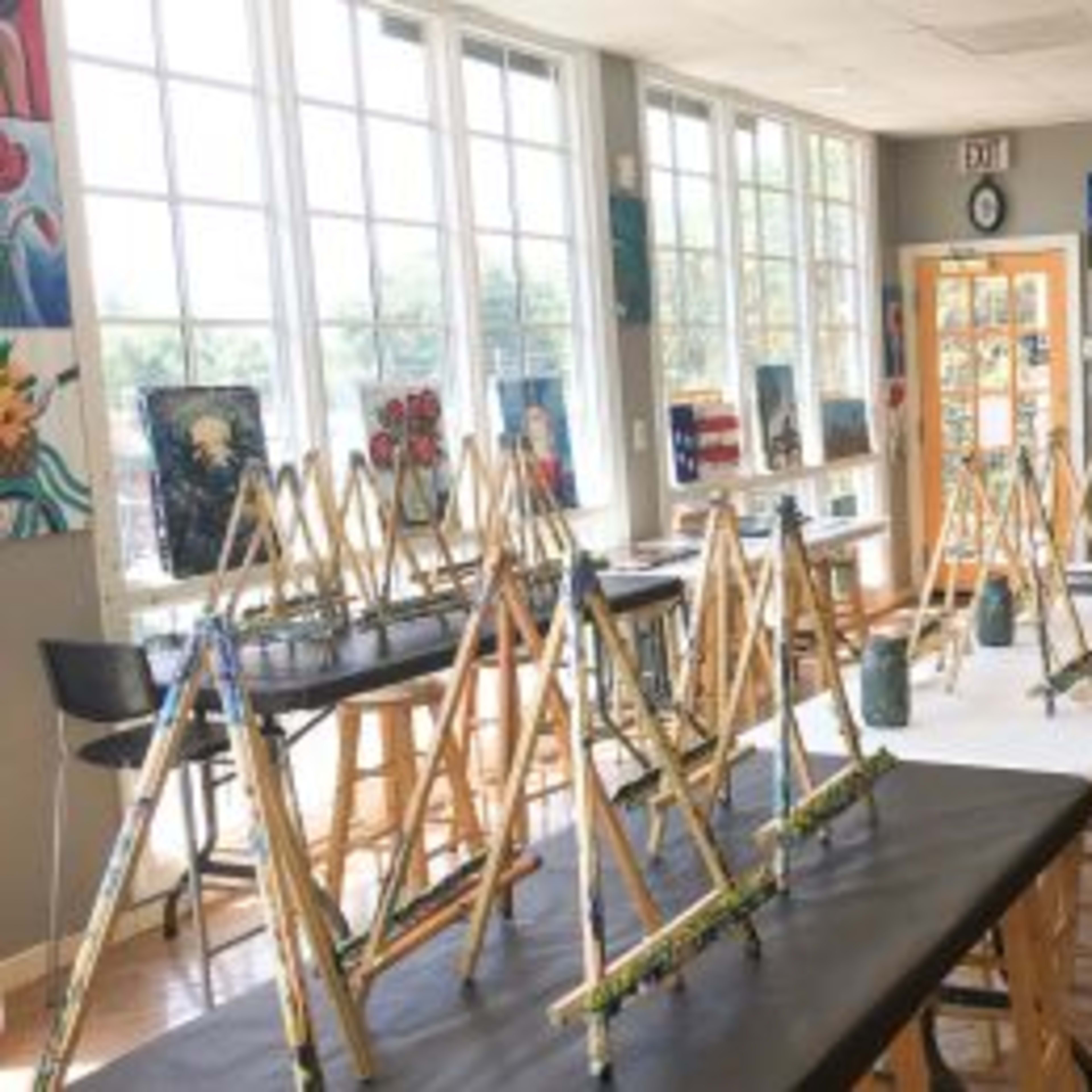 An art studio features several easels set up with canvases and paintbrushes arranged on tables.