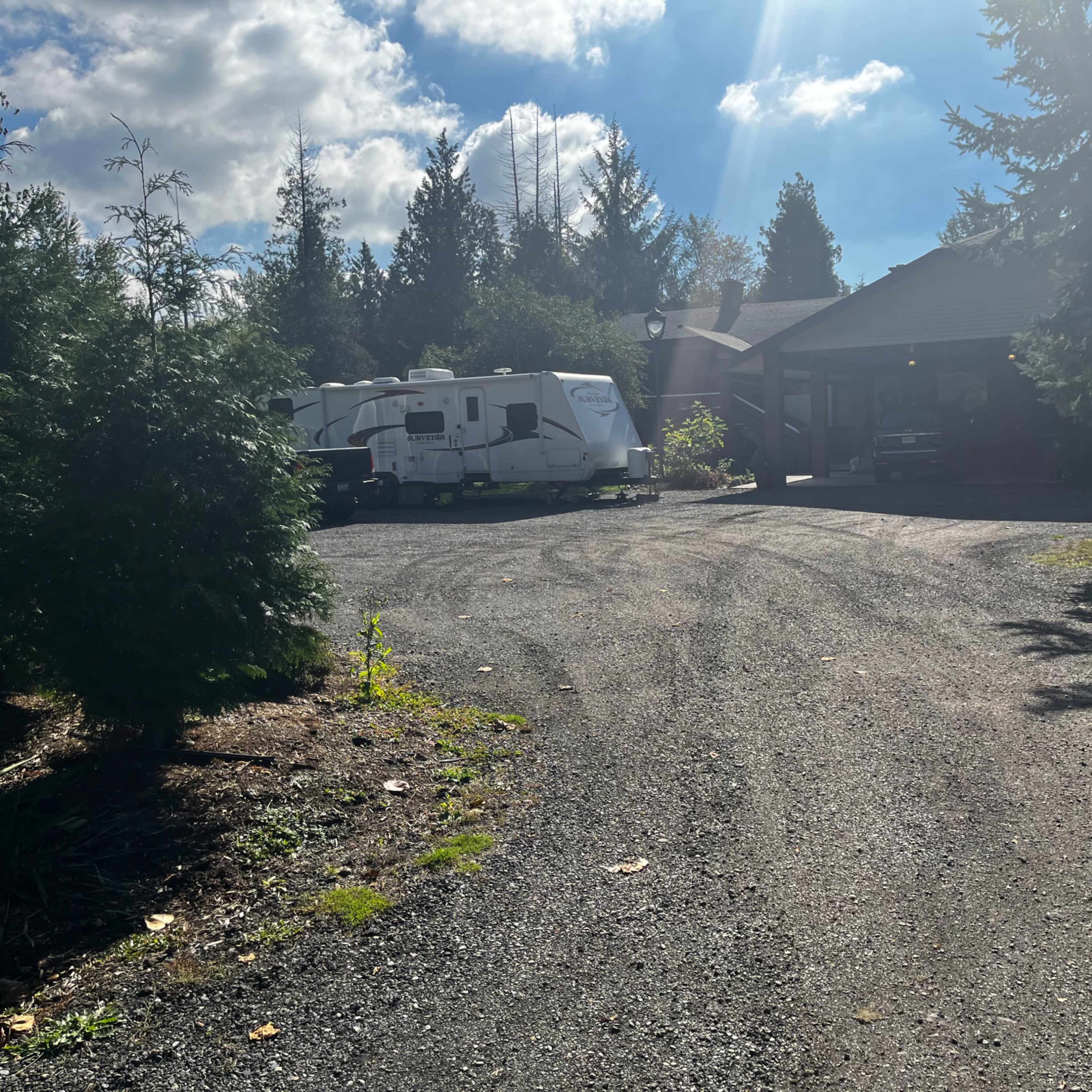 A gravel driveway leads to a house surrounded by trees, with two parked trailers beside the garage.