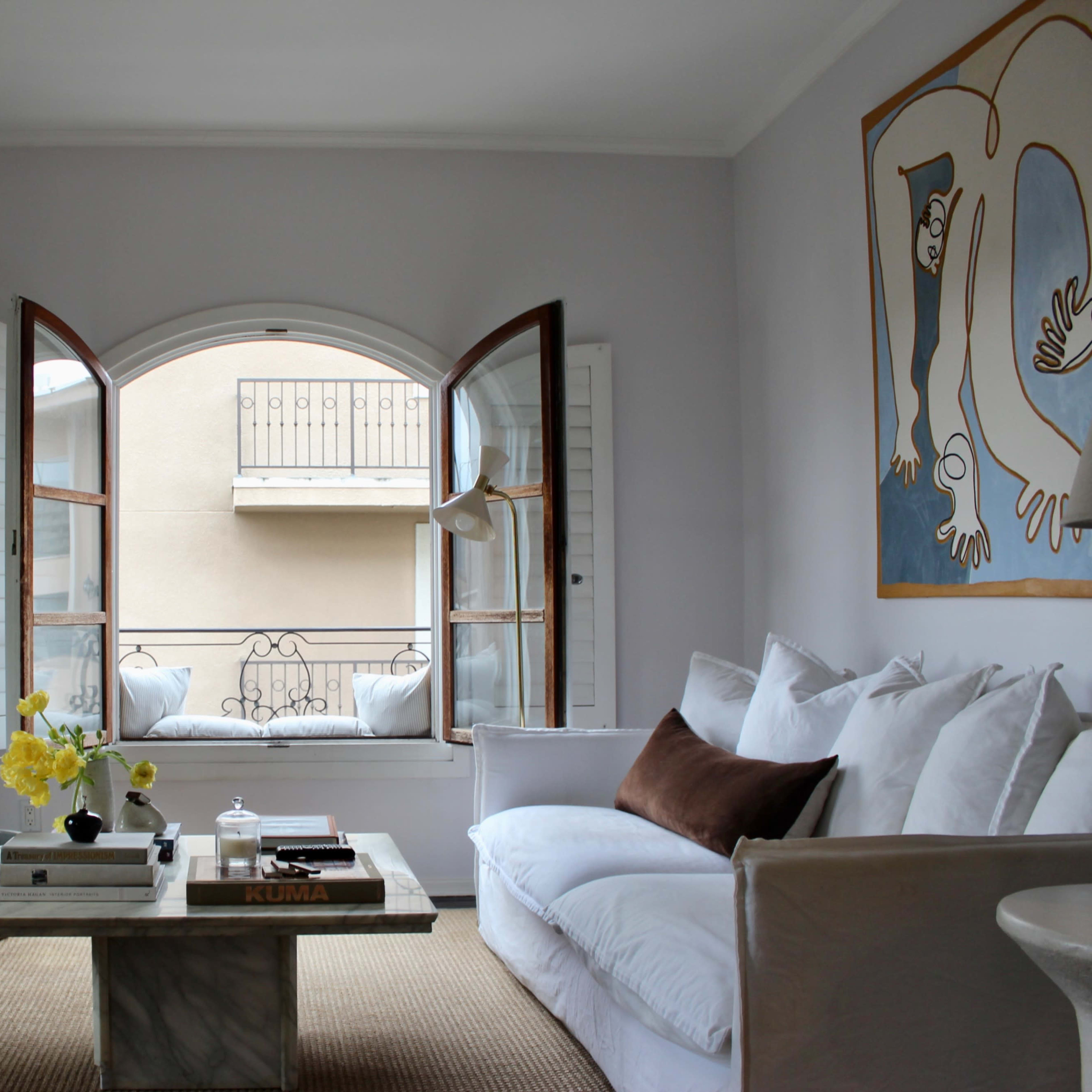 A living room with a stone fireplace, a white sofa, a curved armchair, and an arched window opening to a balcony.