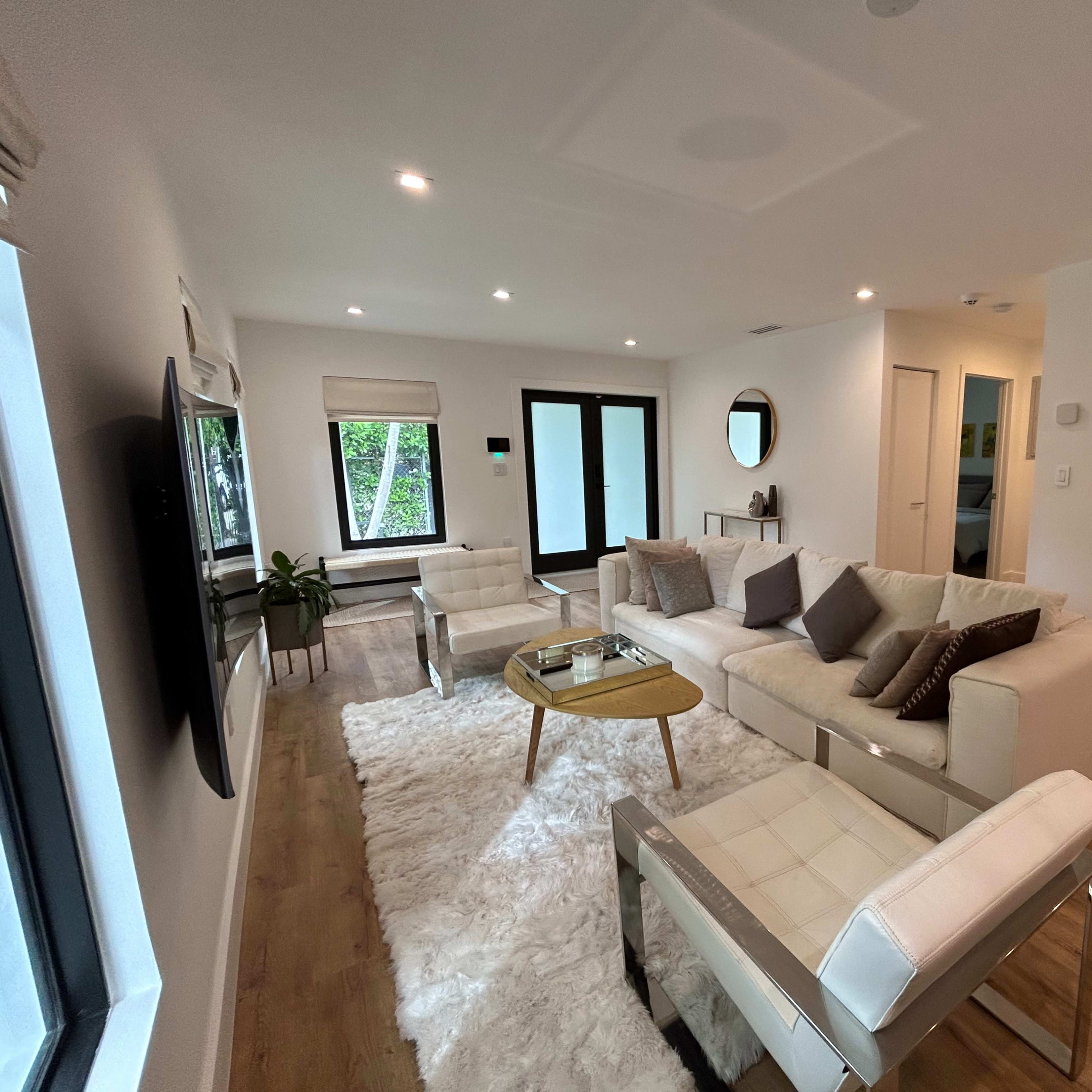 A modern living room features a white sectional sofa, a round coffee table, and large windows that allow natural light to fill the space.