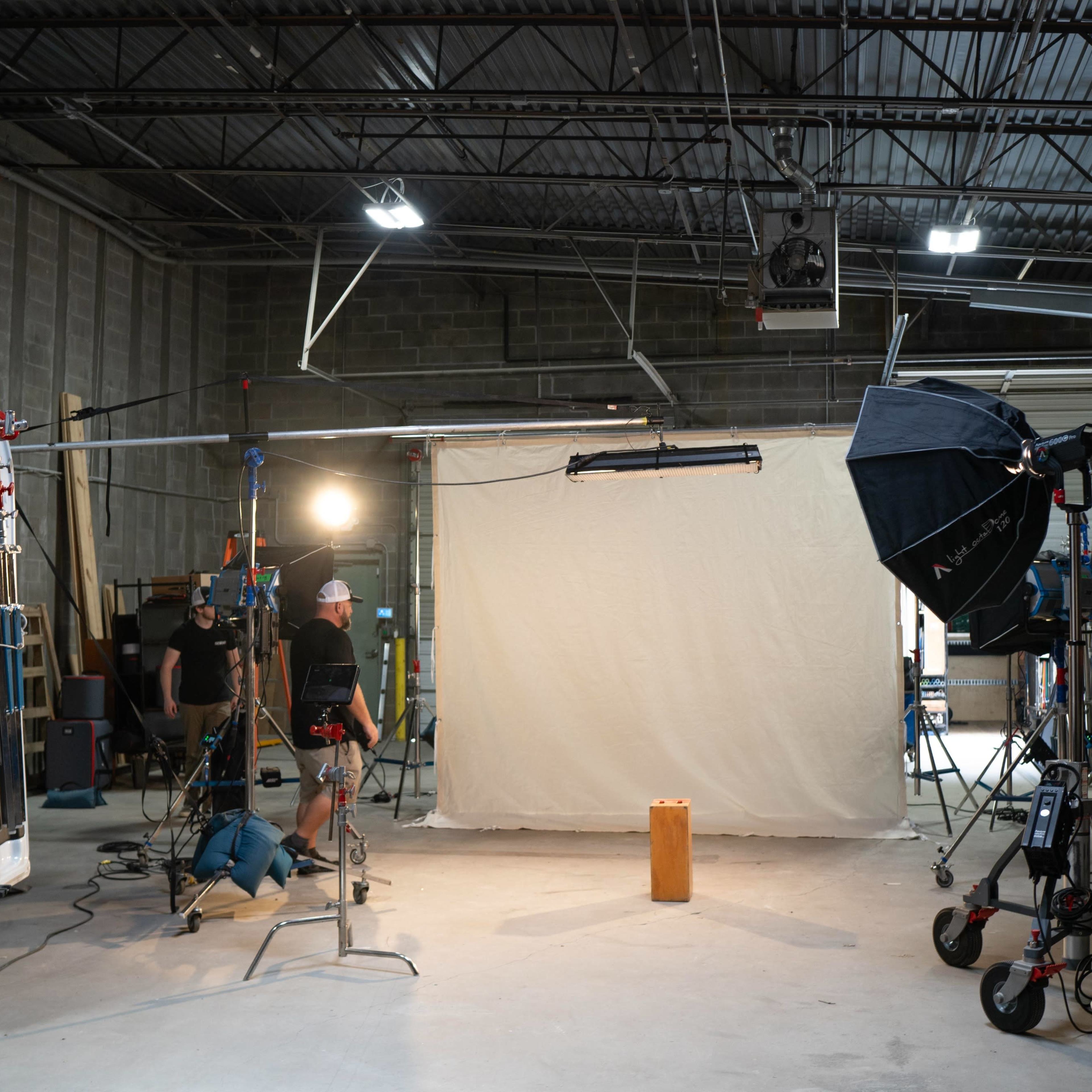 A photography studio setup featuring a backdrop, lighting equipment, and crew members preparing for a shoot.
