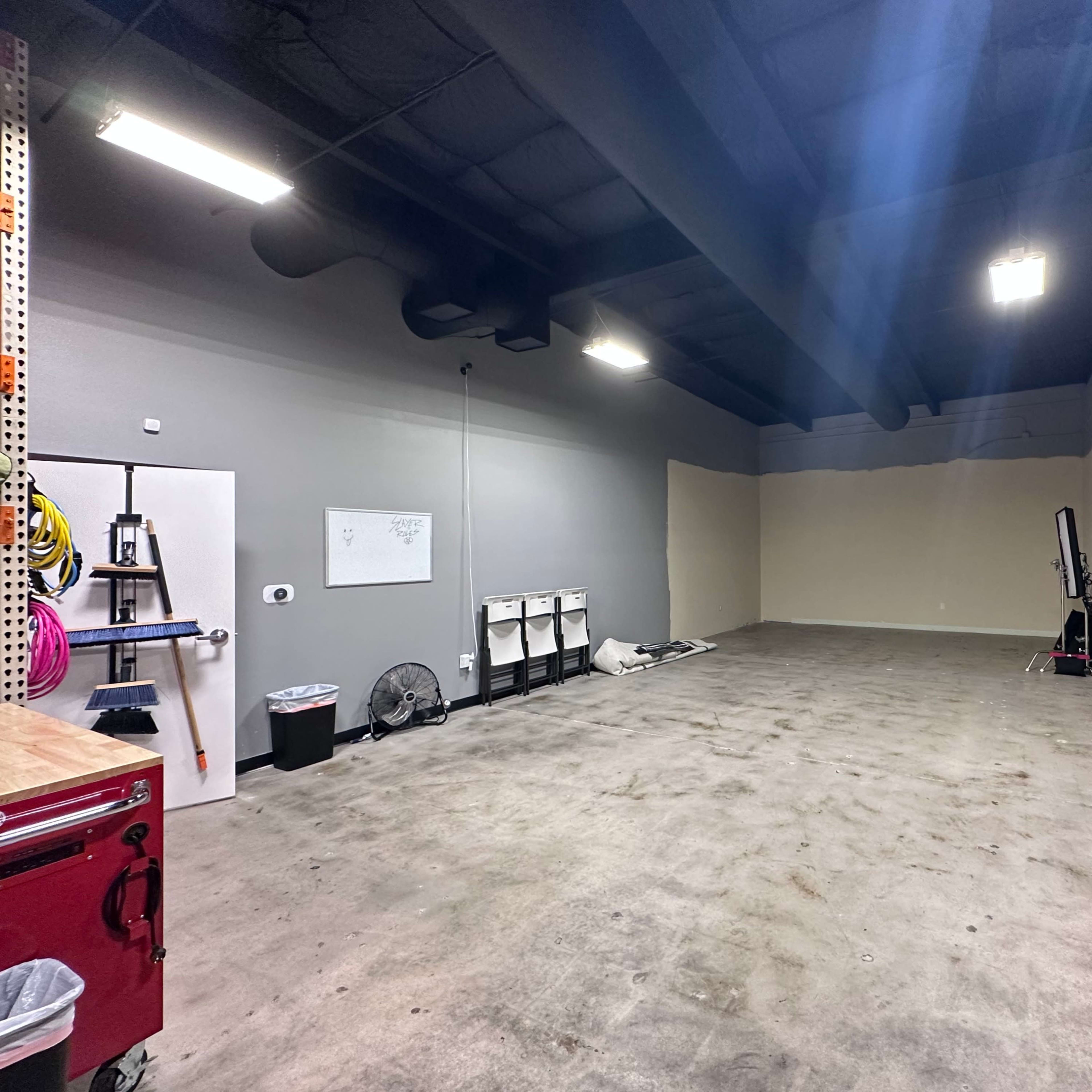A spacious, empty garage or workshop with concrete flooring and unfinished walls, featuring a few storage units and tools along the perimeter.