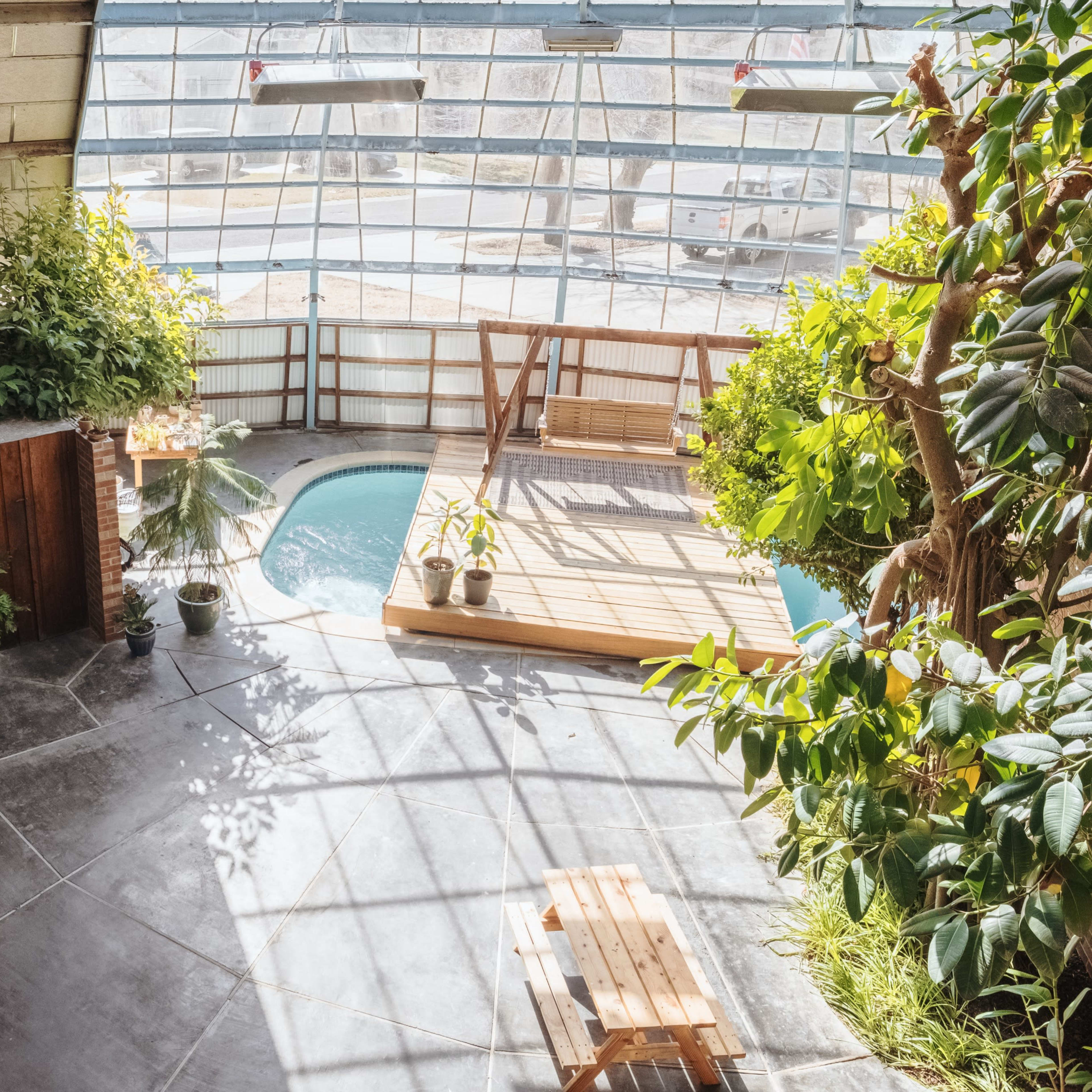 A spacious indoor area with a wooden deck, a small pool, lush greenery, and large windows allowing natural light to flood the space.