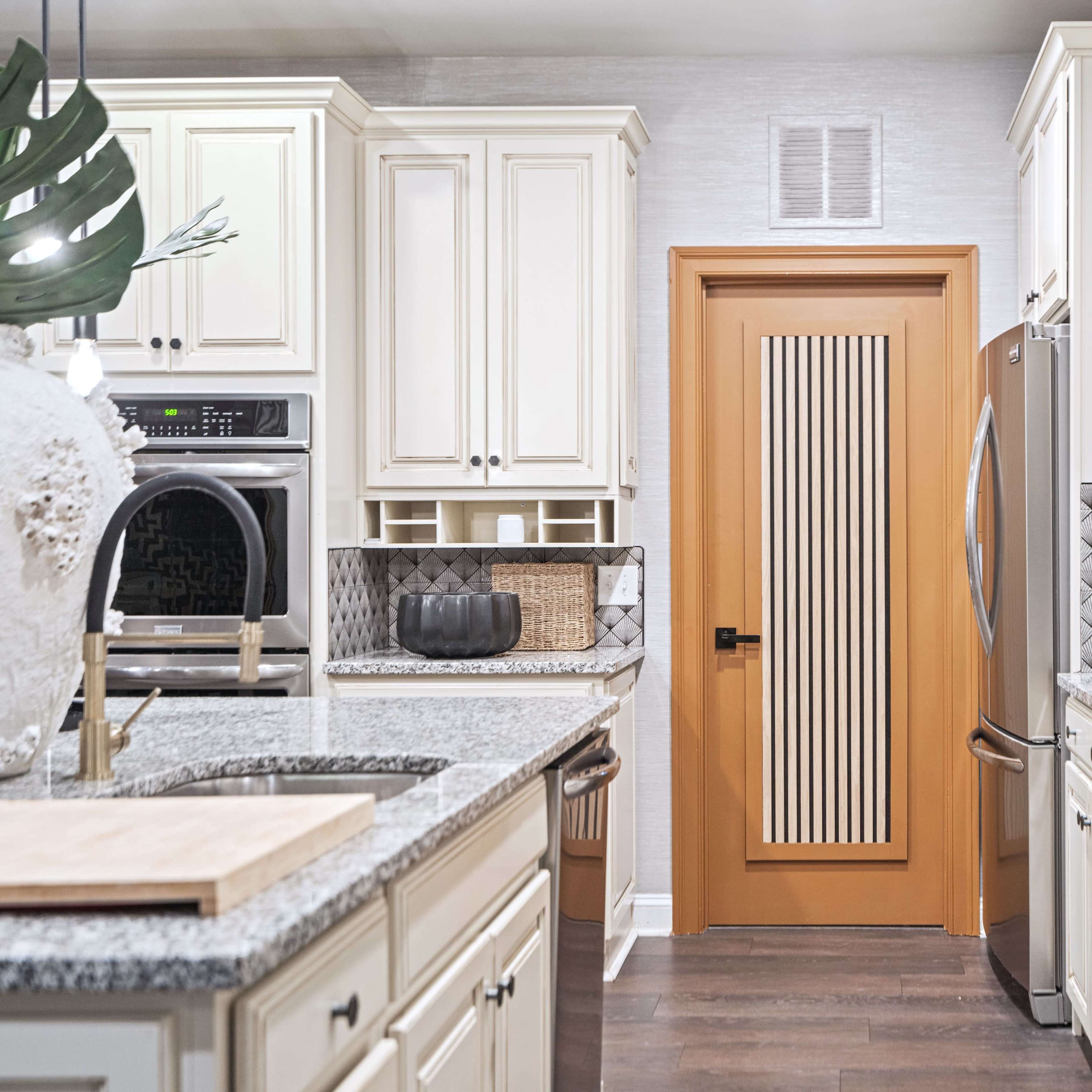A modern kitchen features white cabinets, granite countertops, and a door with vertical slats, leading to another area.