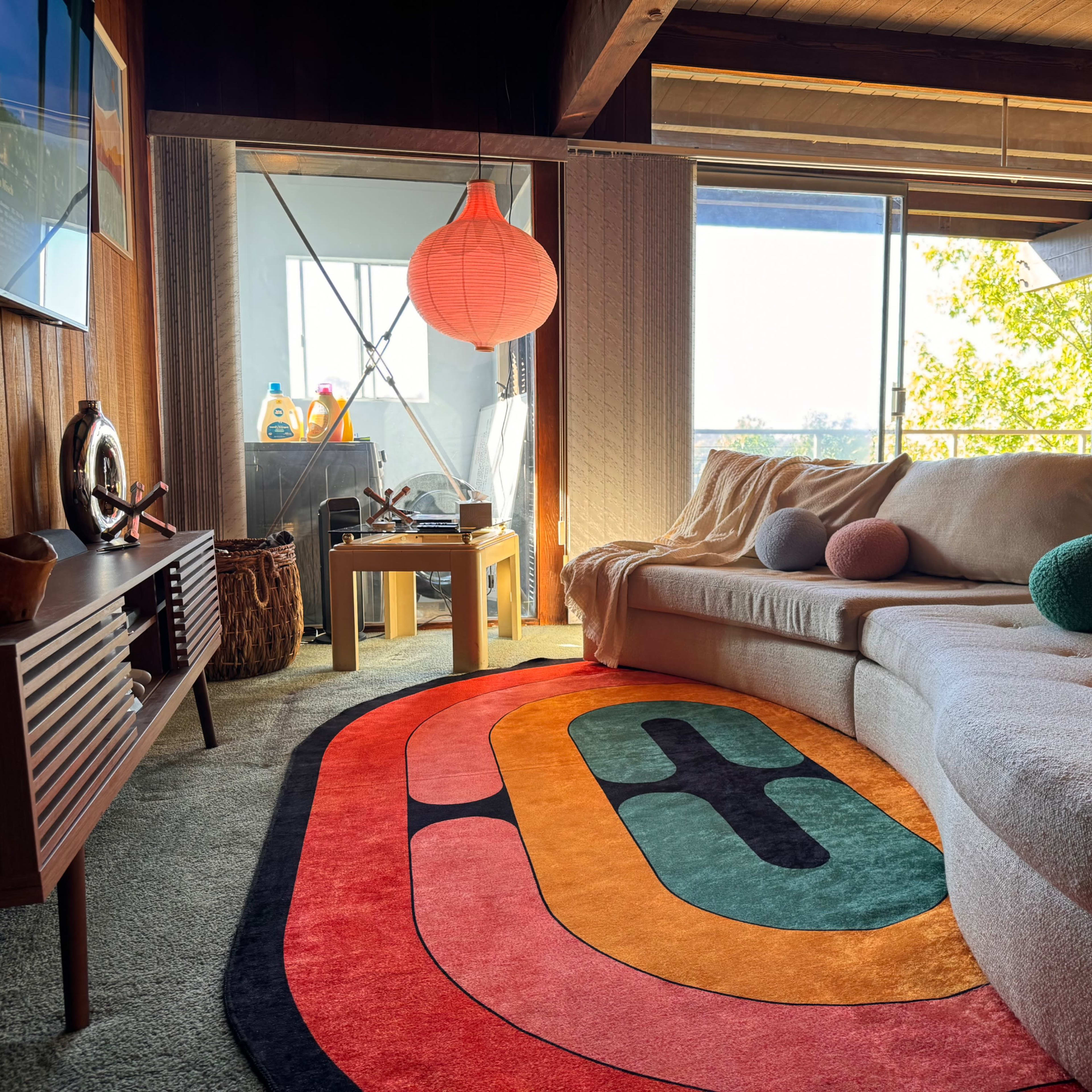 A cozy living room features a large sectional sofa, a colorful area rug, and a window with natural light streaming in.