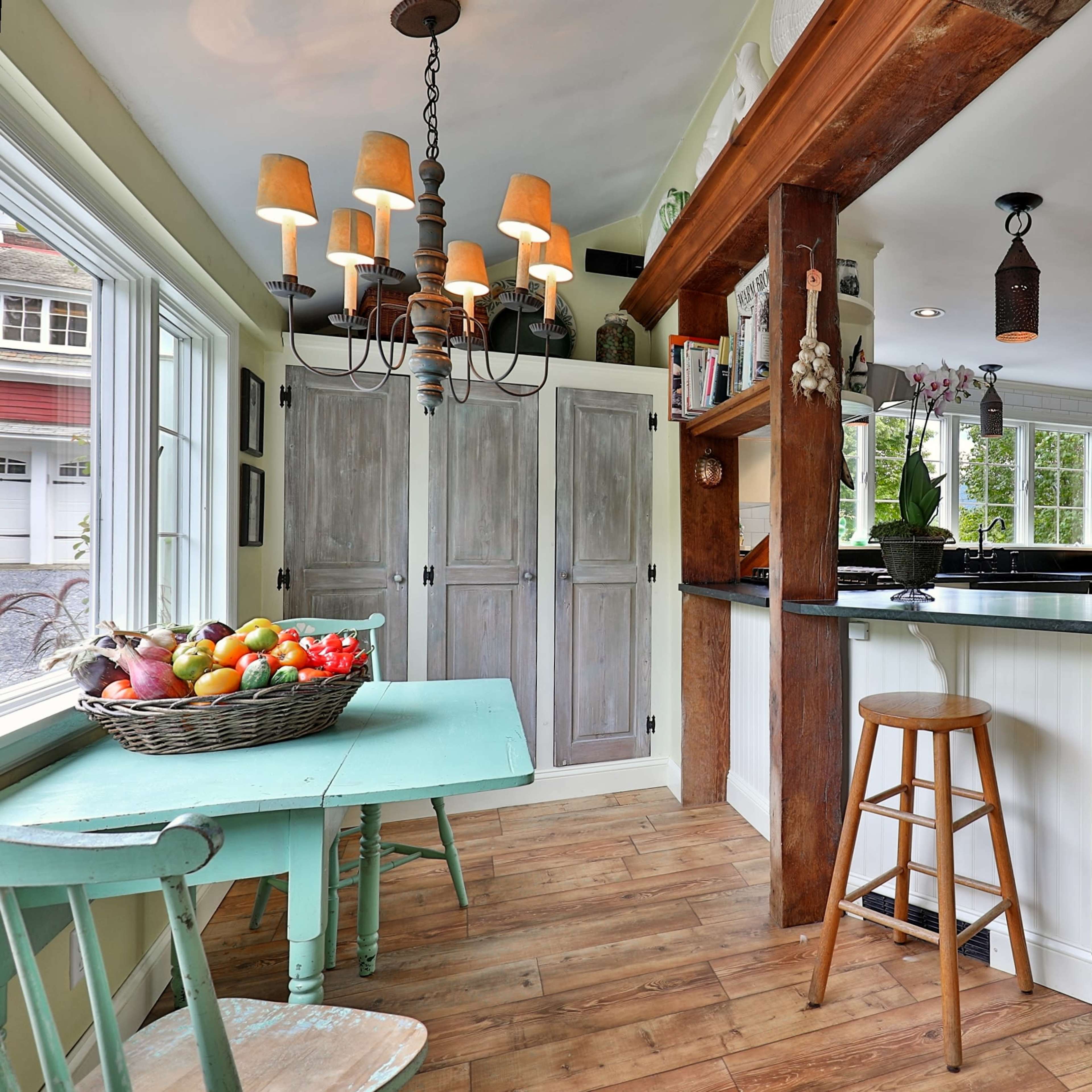 A bright kitchen with a black countertop, wooden beams, and a small turquoise table with two stools.