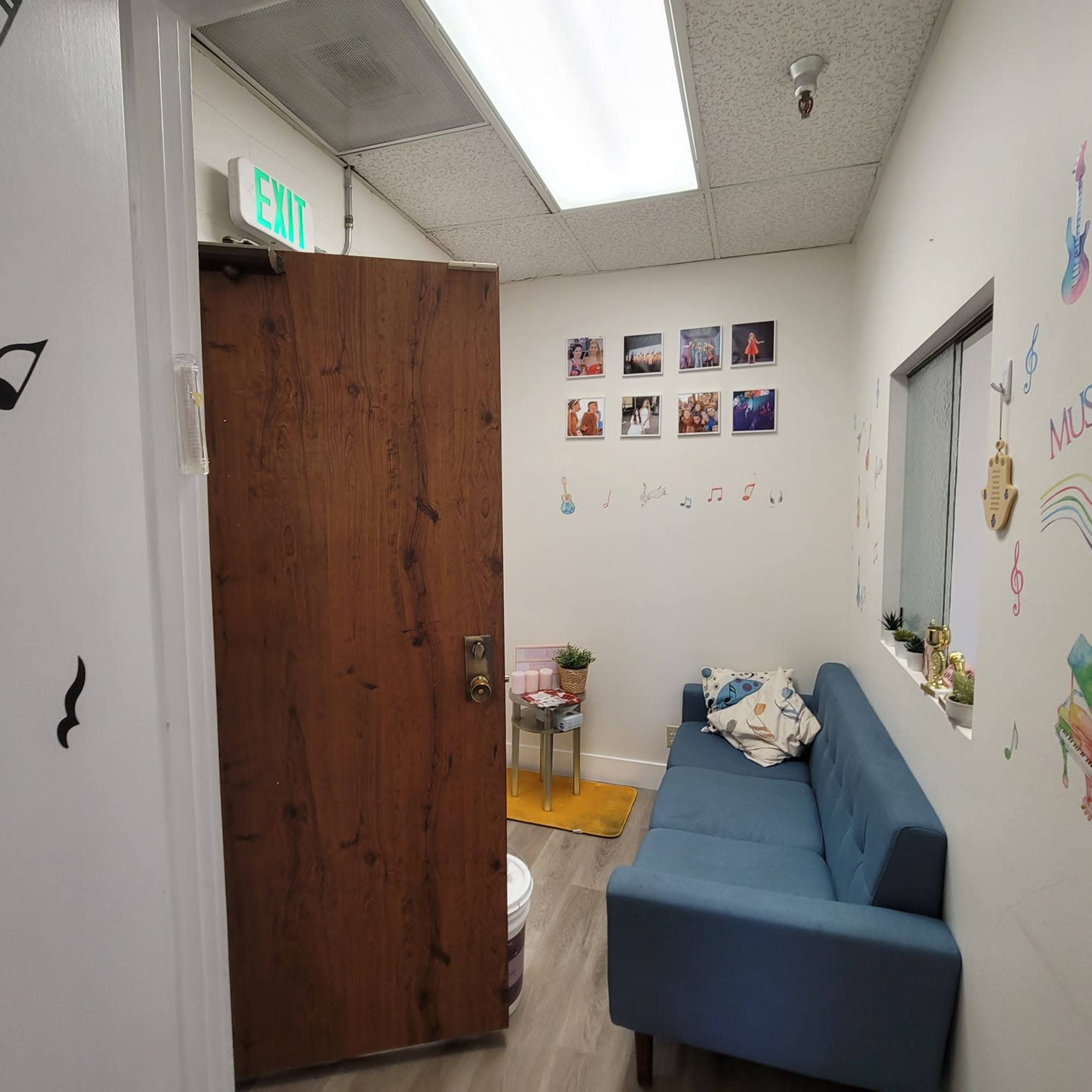A small room with a blue sofa, a door on the left, and decorations including framed photos and musical notes on the walls.