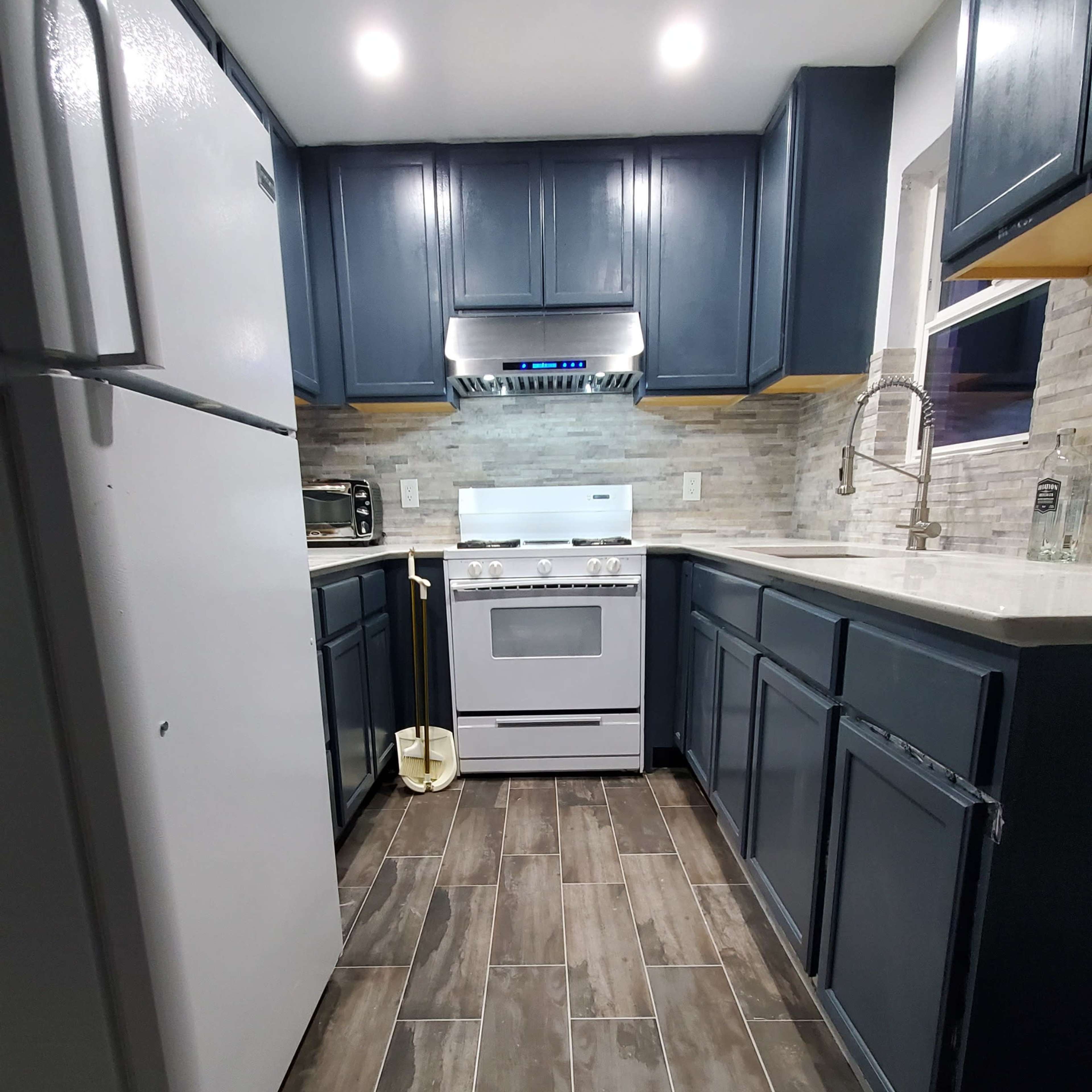 A modern kitchen features a white stove and refrigerator, dark blue cabinets, and tiled flooring arranged in a straight layout.