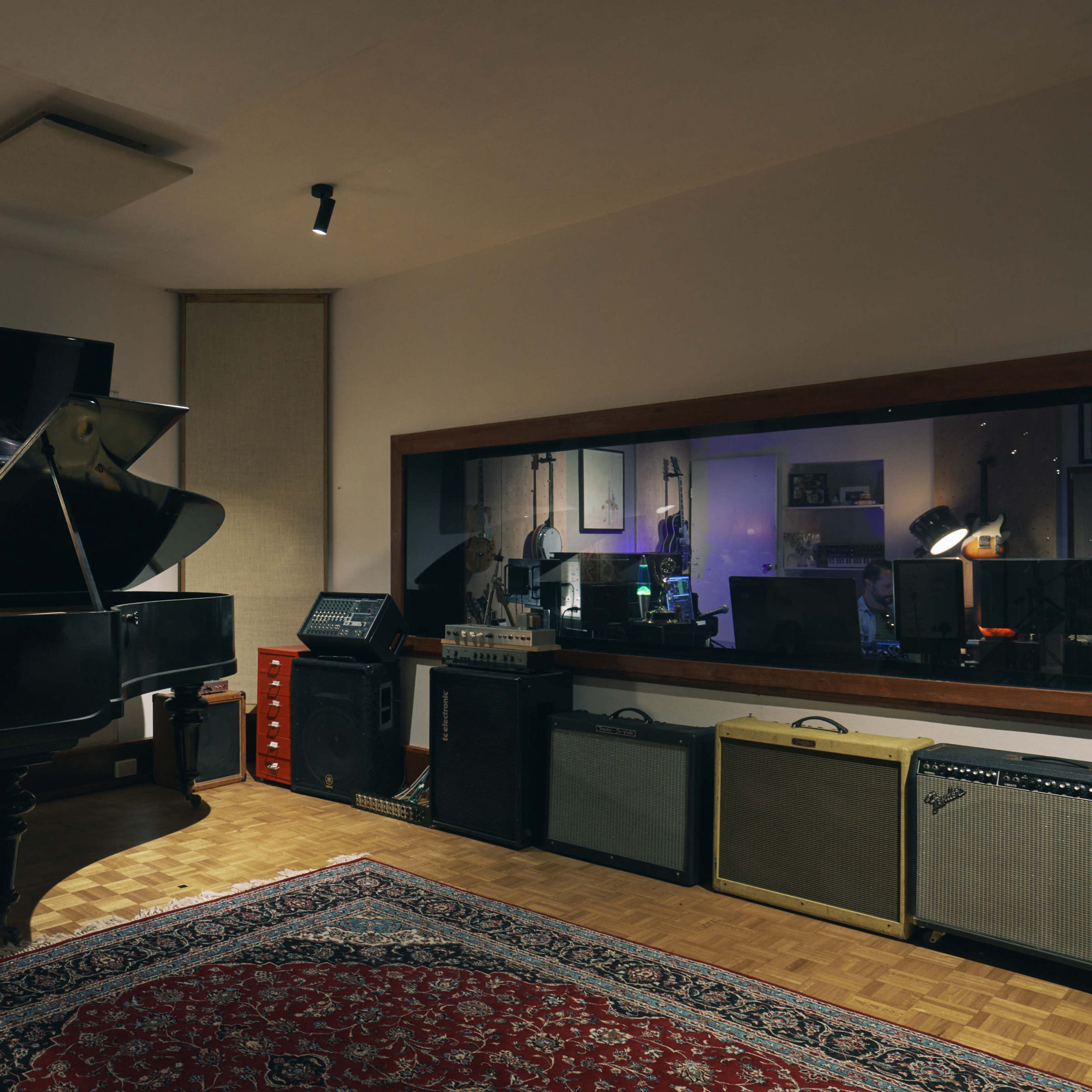 A music studio with a grand piano, recording equipment, and a plush rug on a wooden floor.