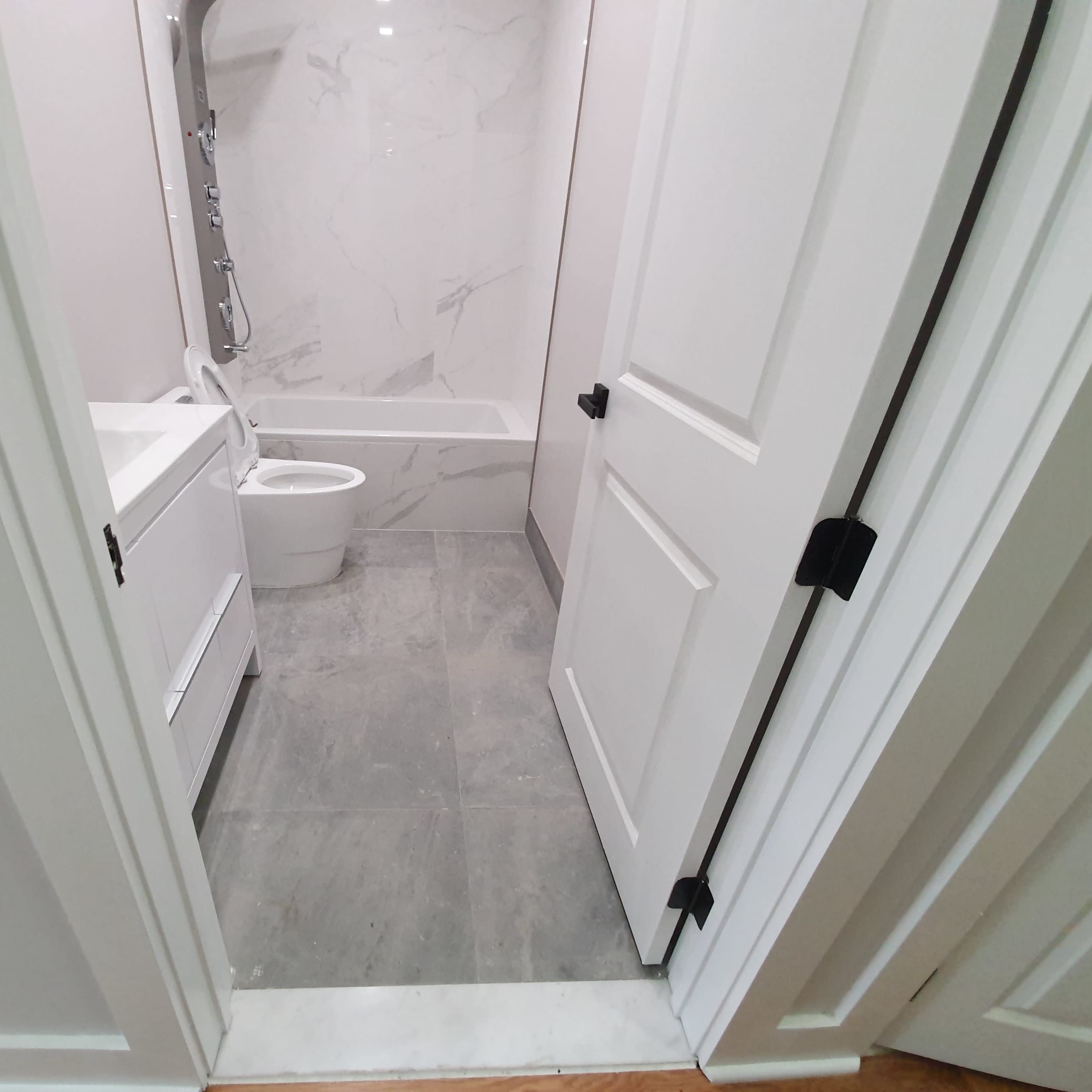 A bathroom with a bathtub, white vanity, and a toilet, viewed from an open doorway.