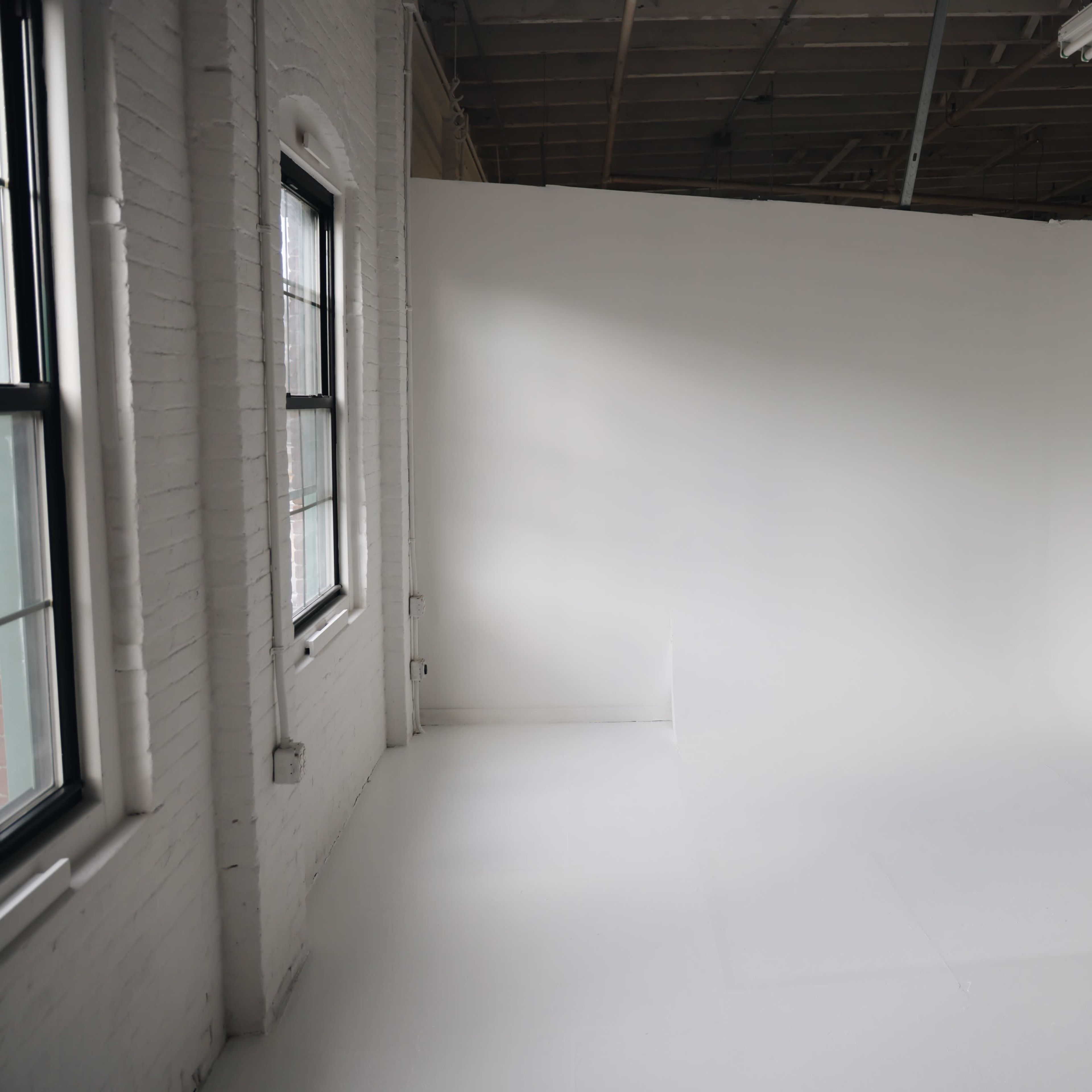 An empty, well-lit studio space with white walls and a seamless white floor.