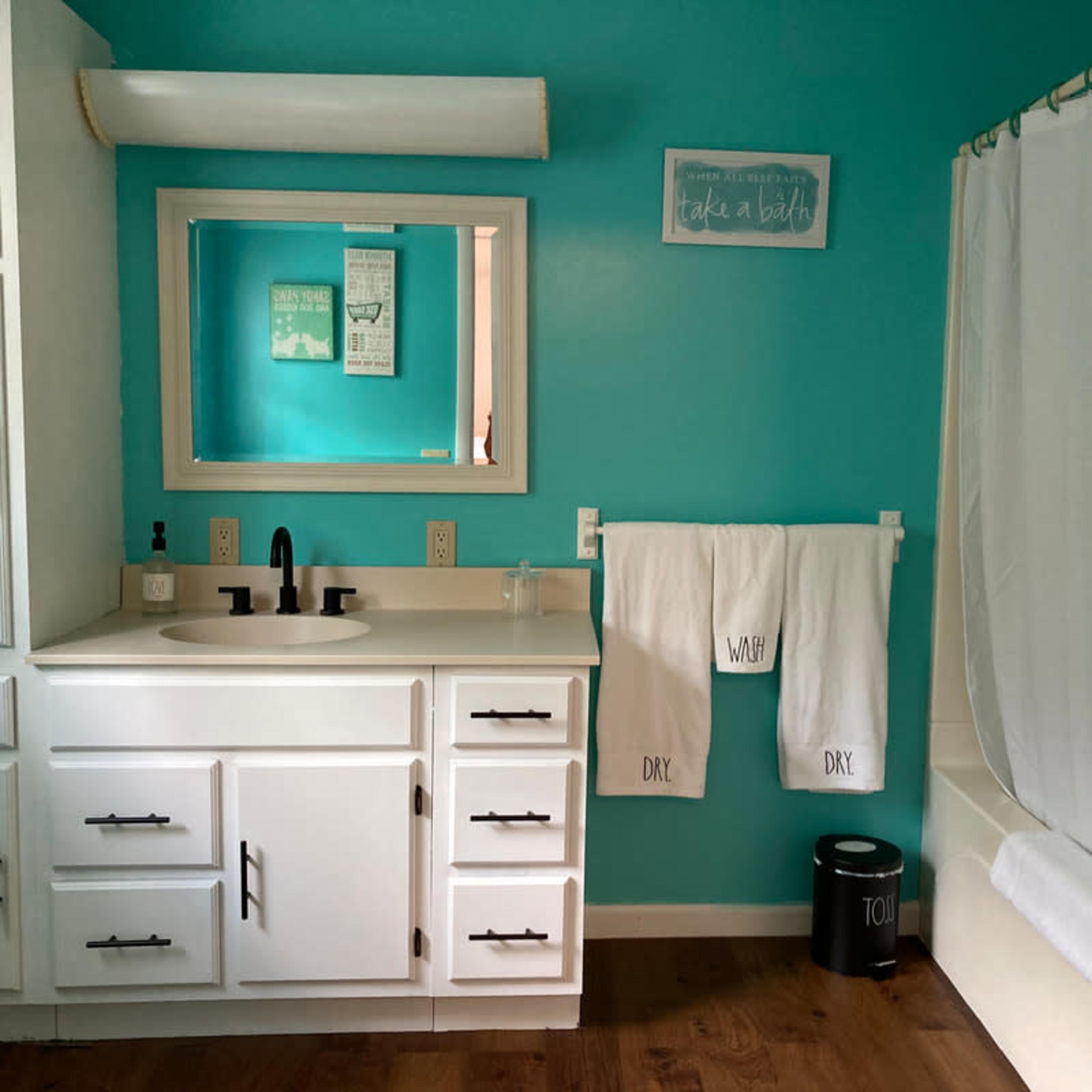 A bathroom with teal walls, a white bathtub, a sink with a large mirror above it, and neatly hung white towels.