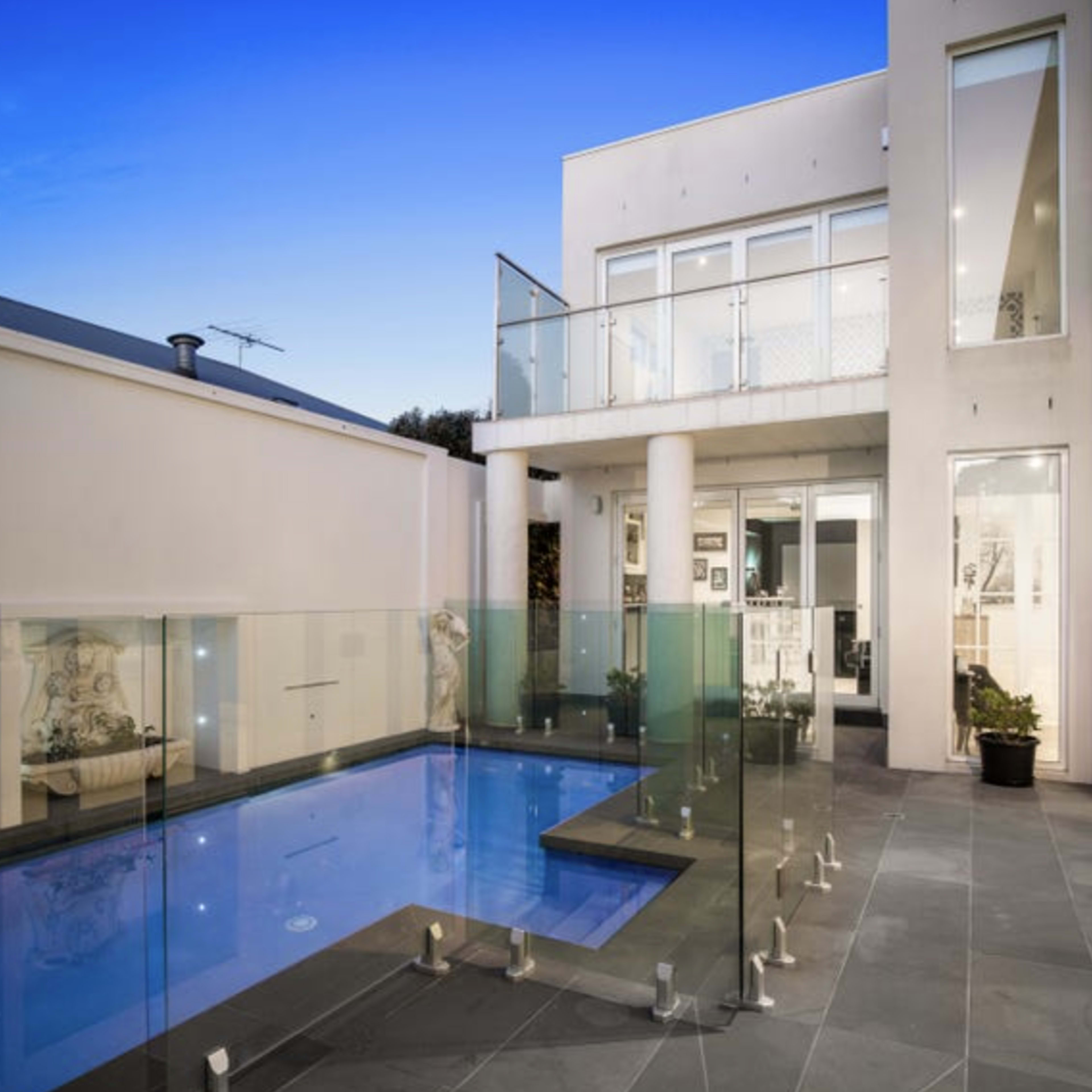 A modern house with a glass-enclosed pool area and multiple large windows under a twilight sky.