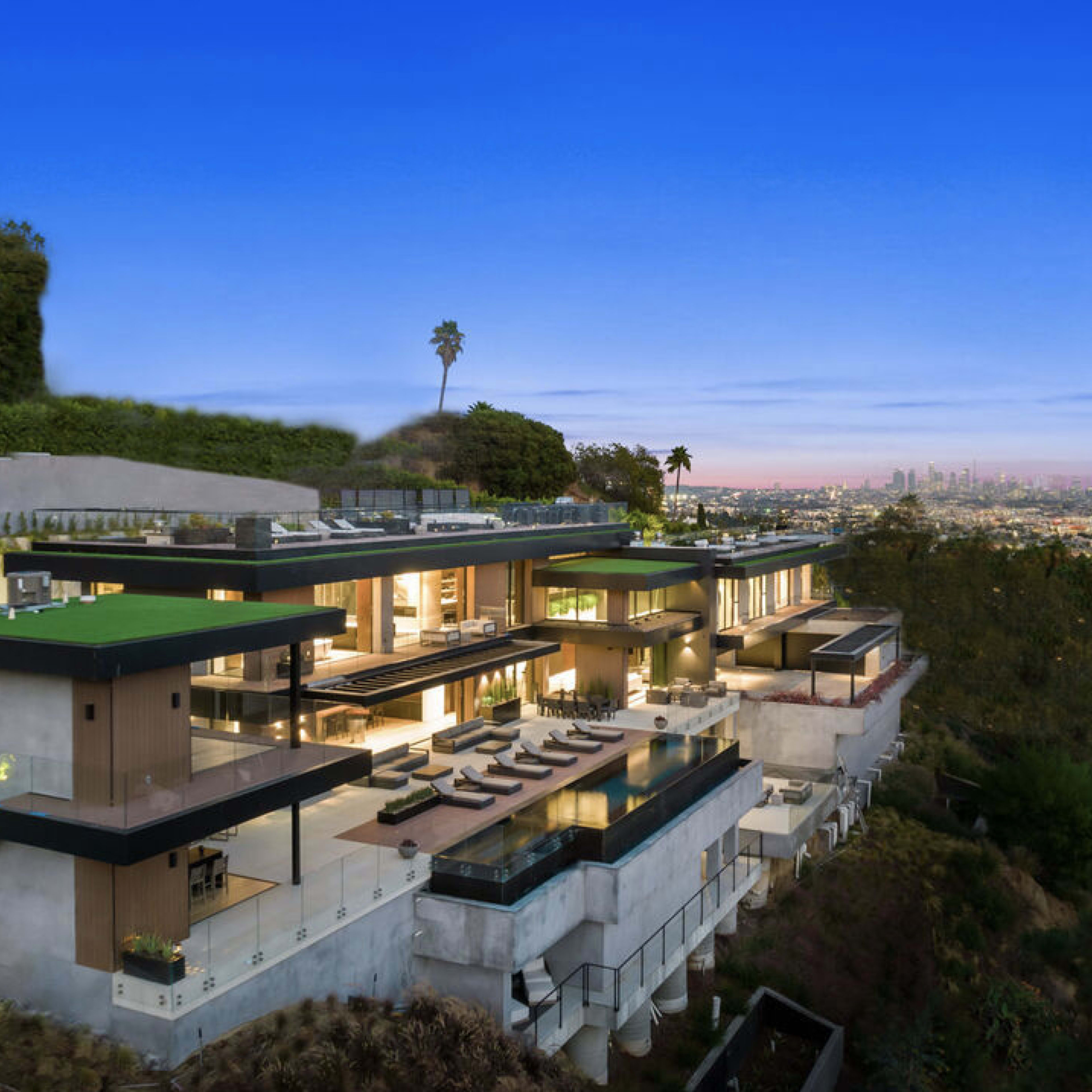 A modern multi-level house features large glass panels and a swimming pool, set on a hillside with a view of the city skyline.