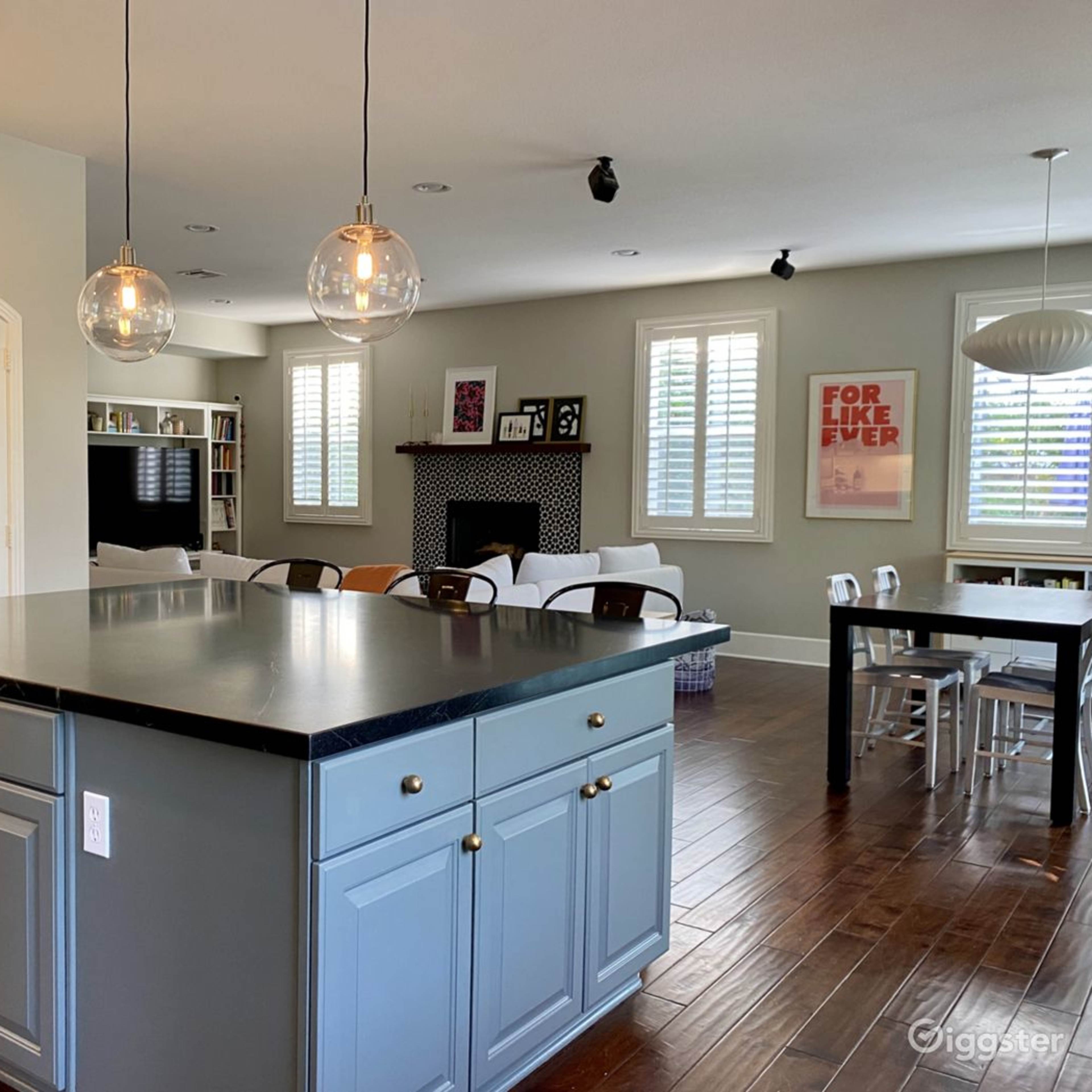 A modern kitchen with an island featuring blue cabinetry, pendant lights, and a dining area in an adjacent room.