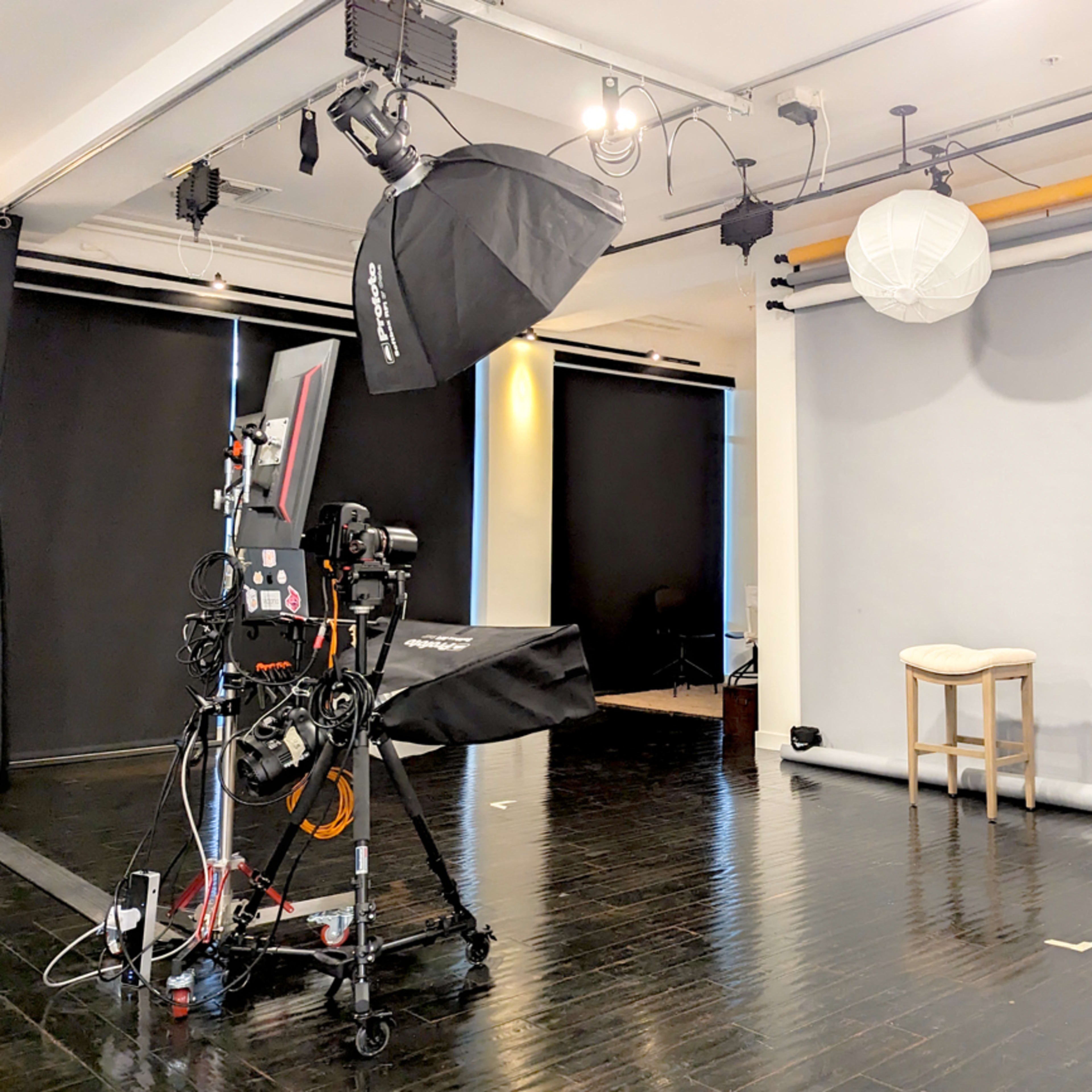 A photography studio with a camera setup, softboxes, and a neutral gray backdrop.