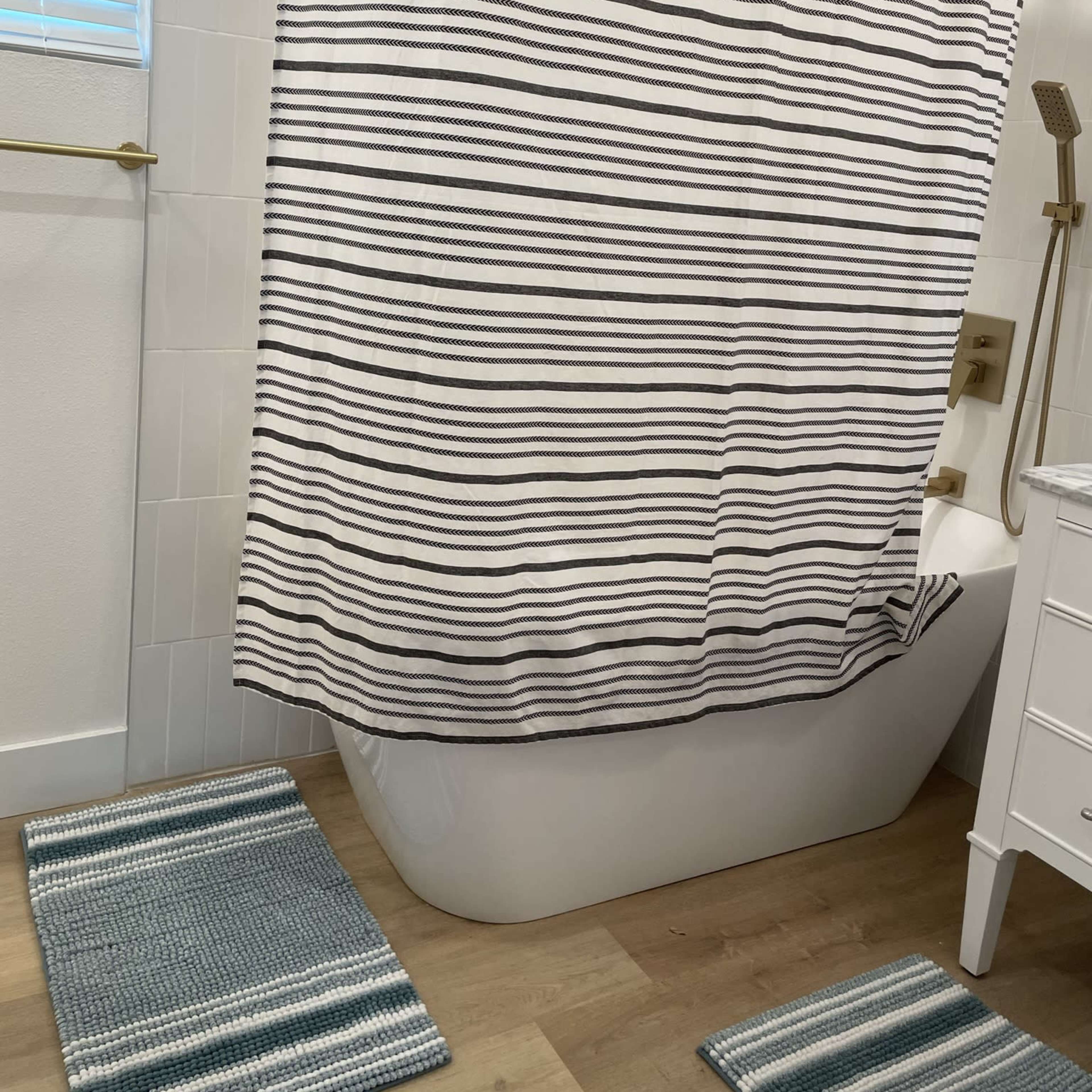 A bathroom featuring a bathtub with a striped shower curtain and two striped bath mats on the floor.
